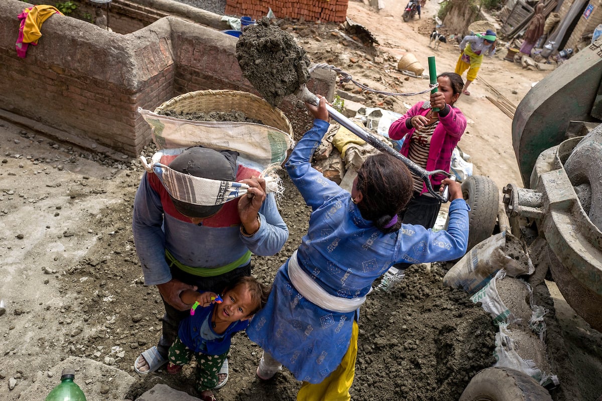 A construction worker takes care of his young daughter while two women load his basket with sand in Bhaktapur, Nepal.