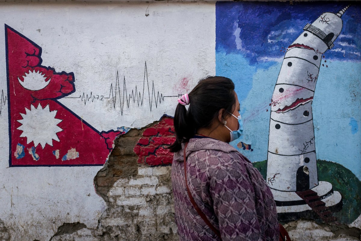 A woman passes in front of a painting representing the destruction of the Dharahara tower in Kathmandu, Nepal.