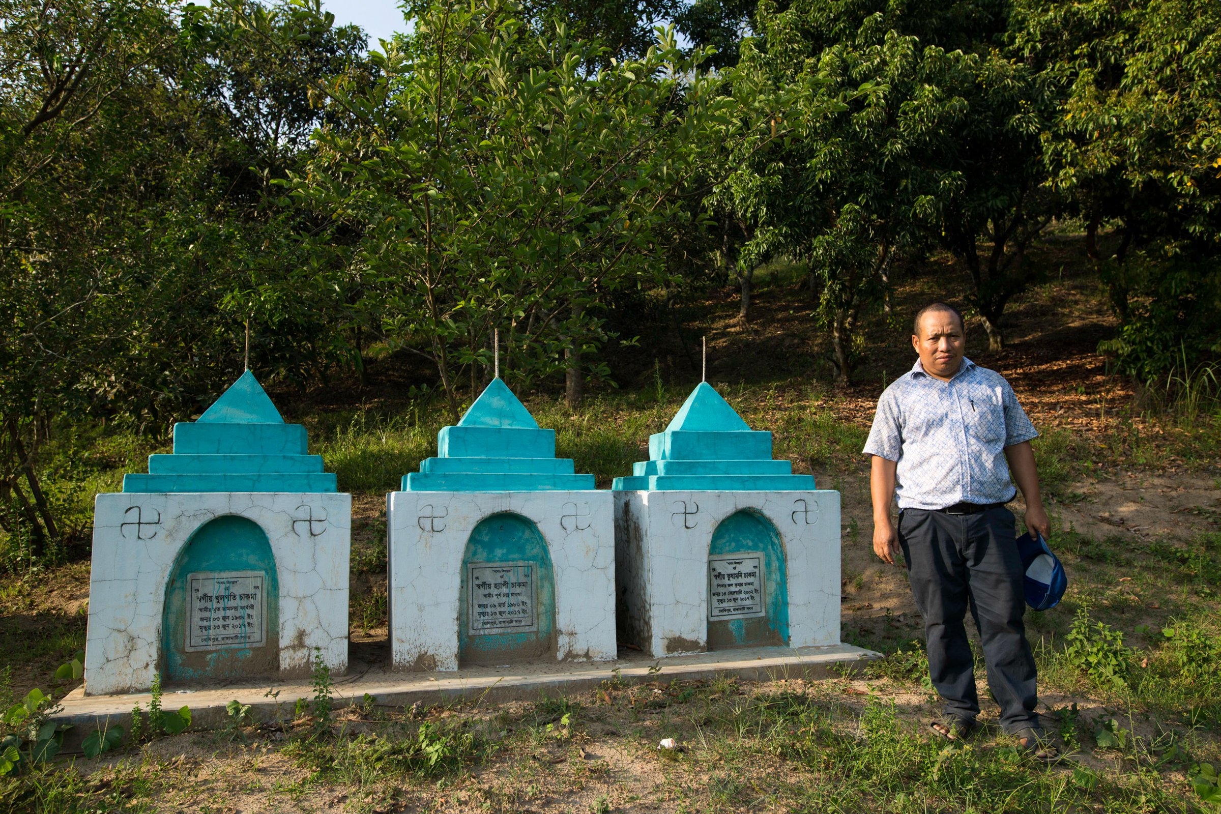 Photo of man in Bangladesh next to grave of relatives who died in a landslide.