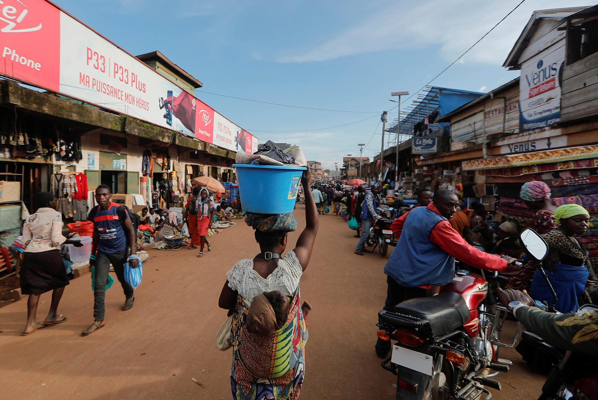 A woman carries a basin with goods through a market in Butembo