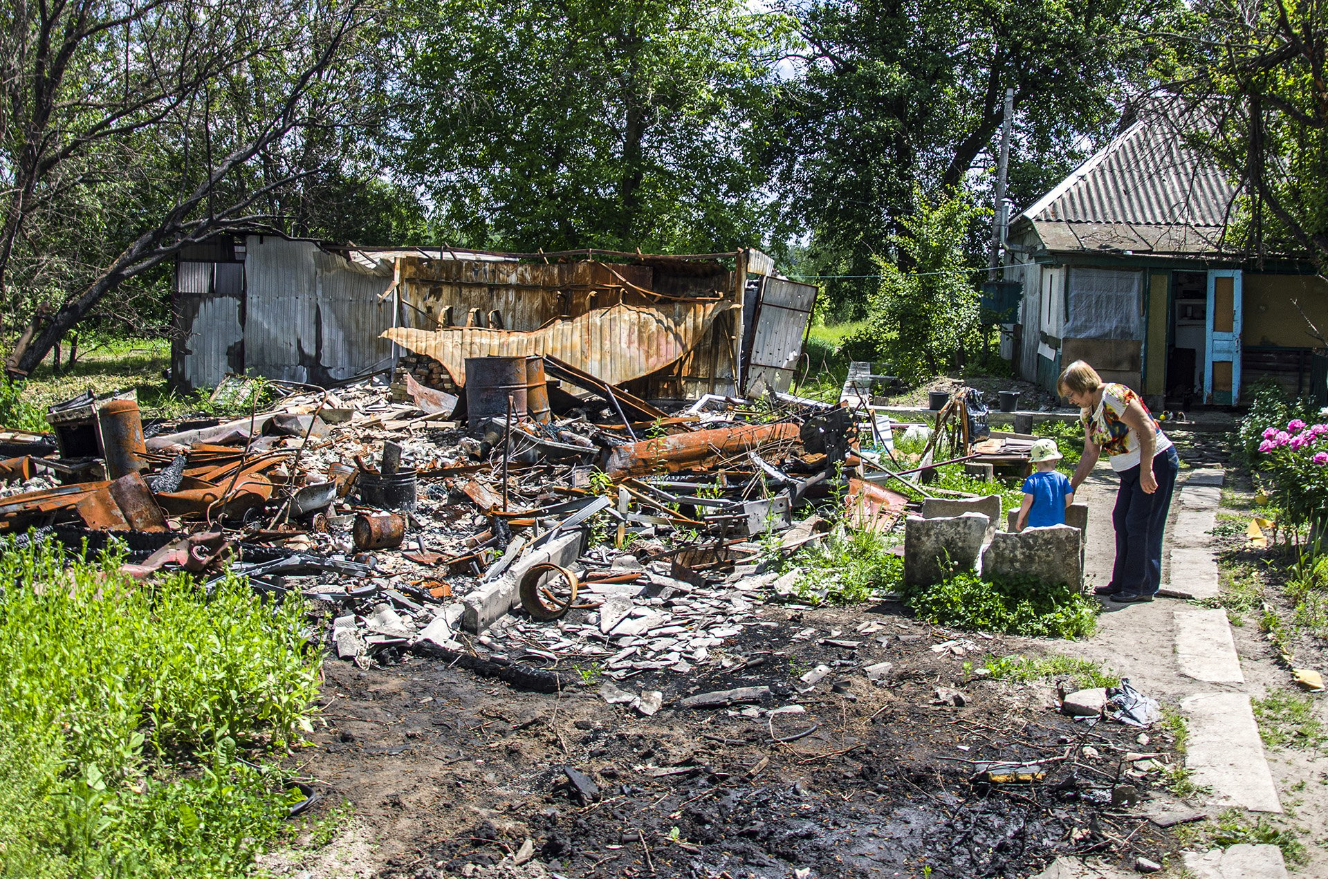 A woman looks at what's left of a building and garden after shelling.