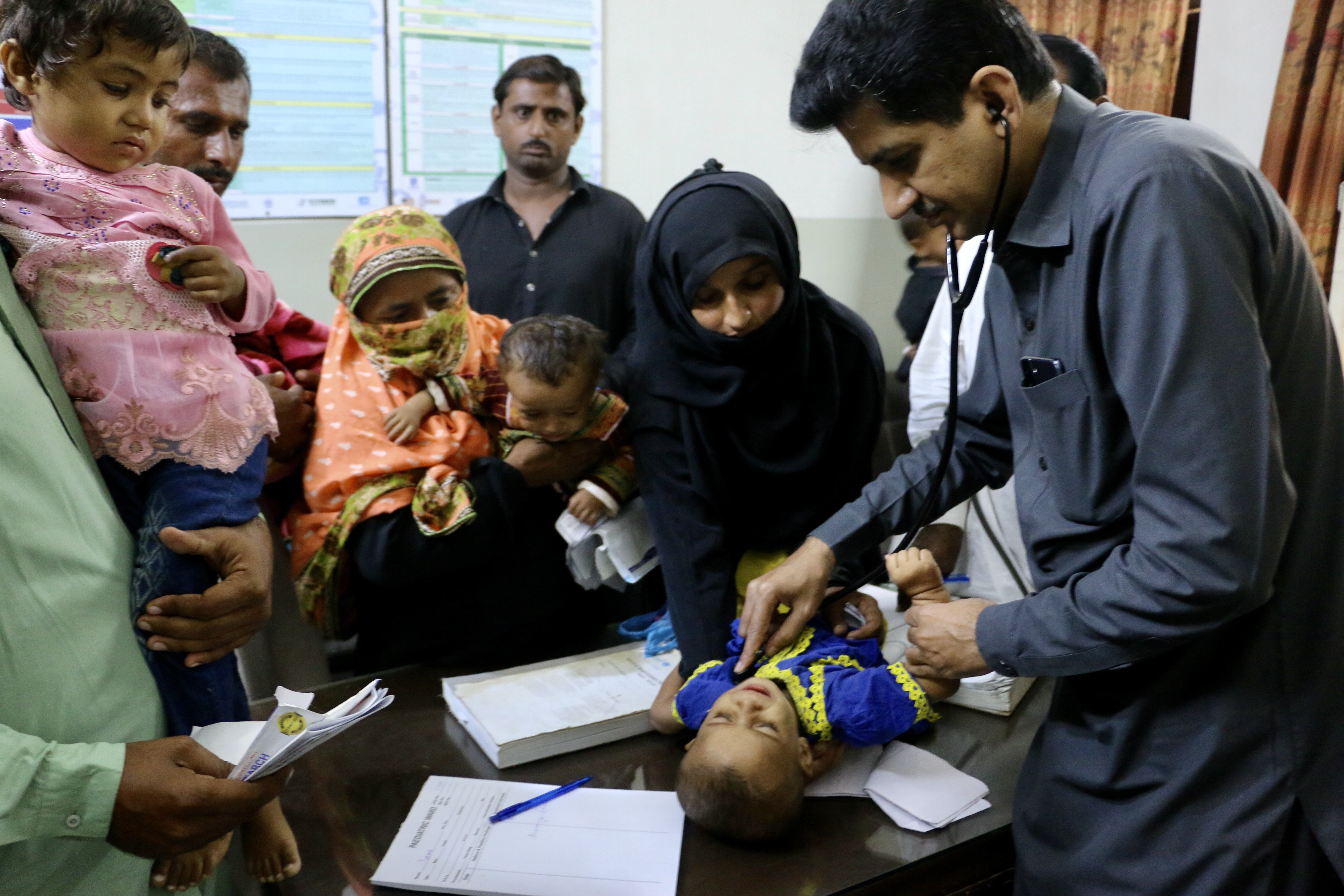 Shabana holds her baby, Lareb, while a paediatrician listens to her vitals. The baby was diagnosed with malaria, which has been spreading amid the floods.