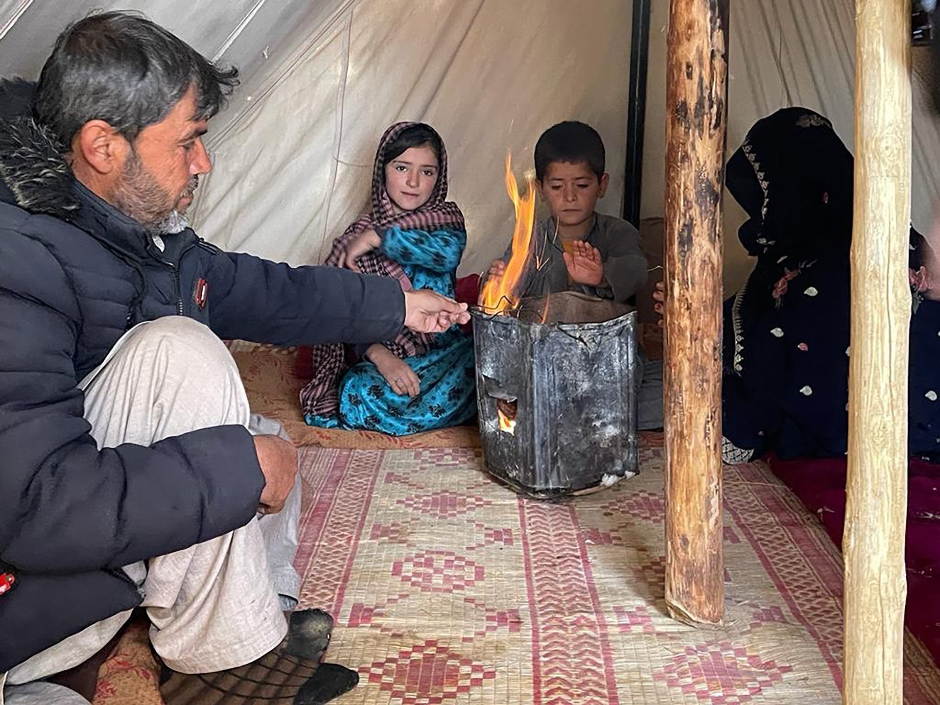 A family sits inside a tent with an open flame.