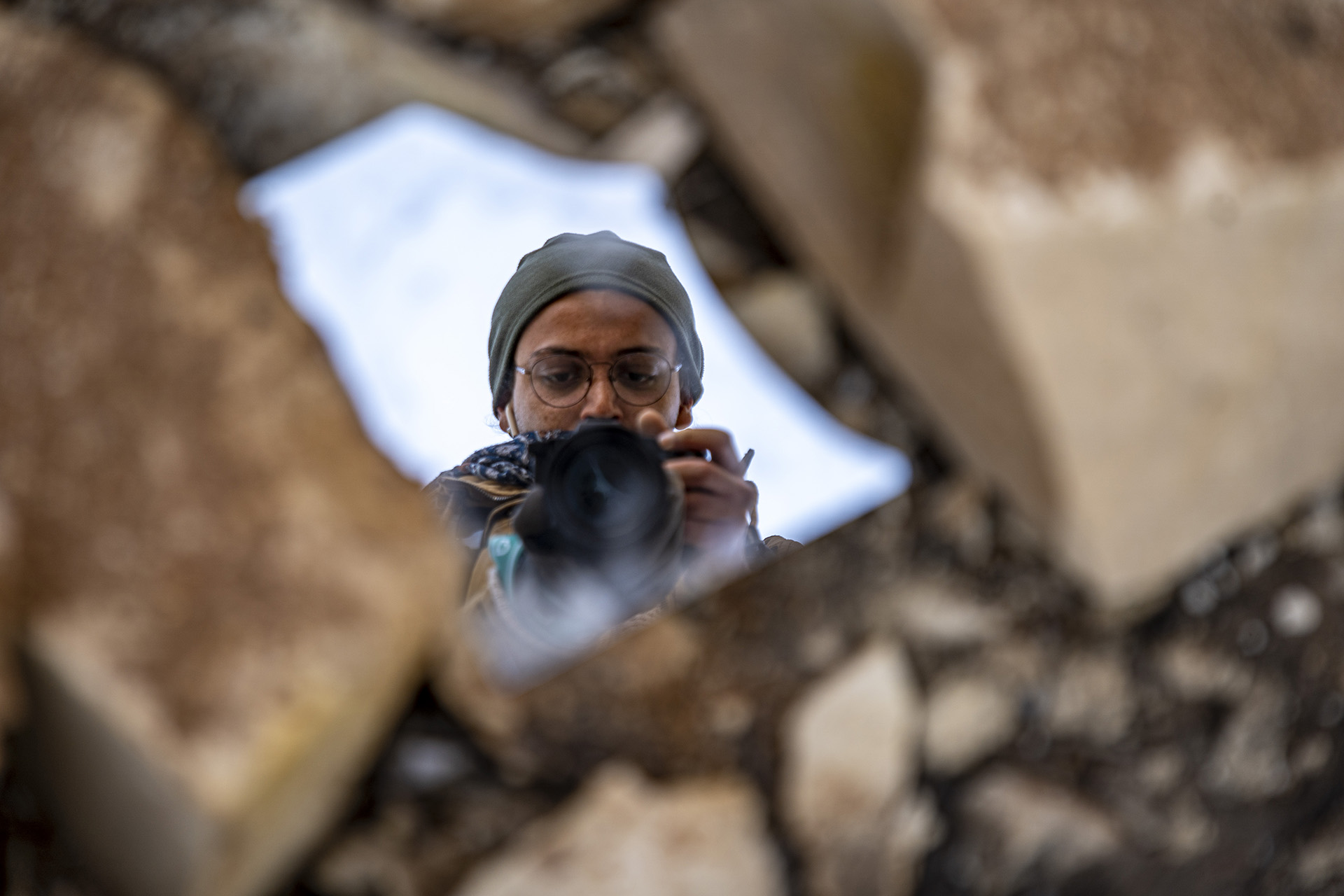 A photographer takes a photo of themselves in a shard of broken mirror