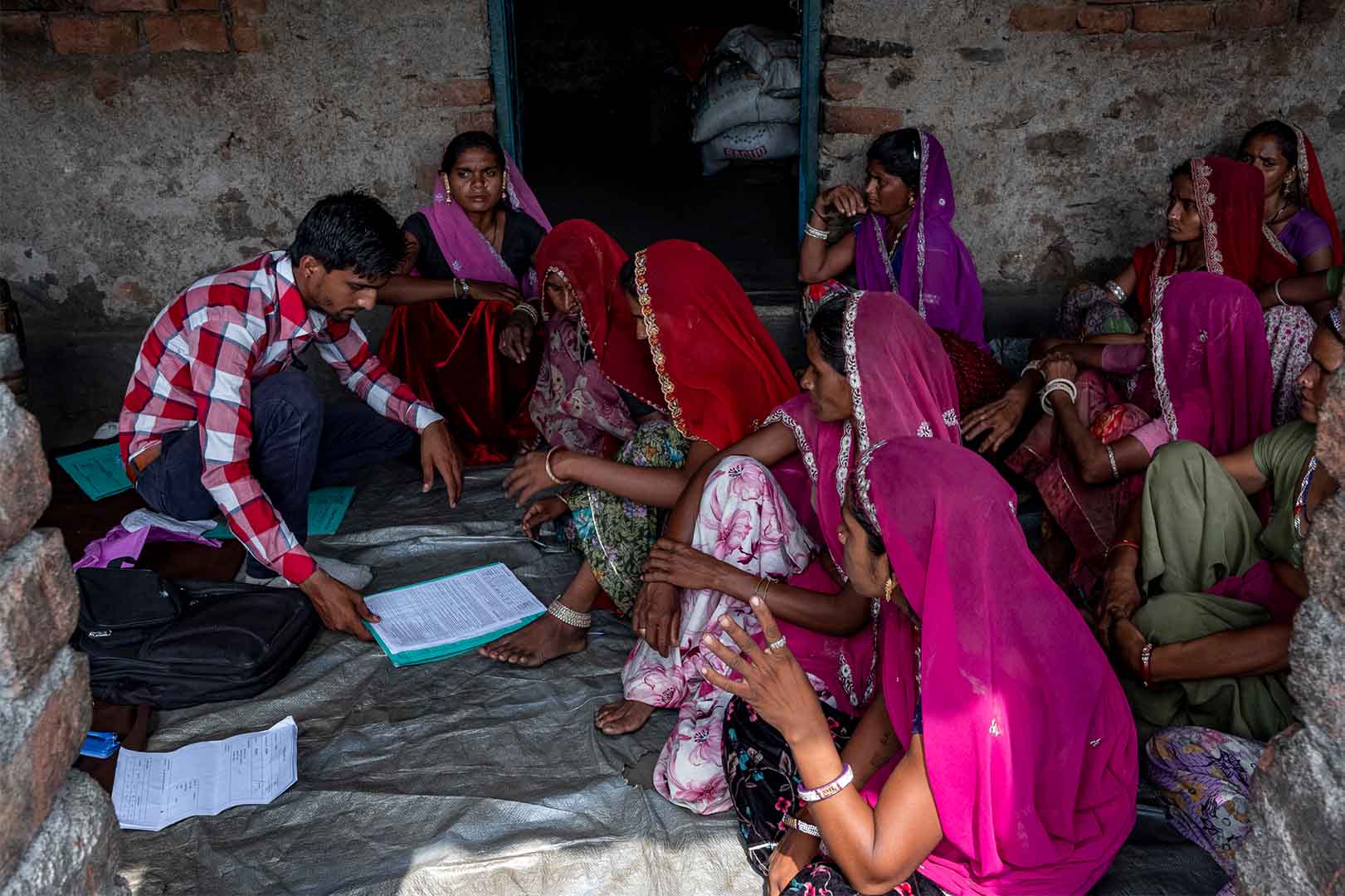 A group of women sit on the floor in discussion with a man.