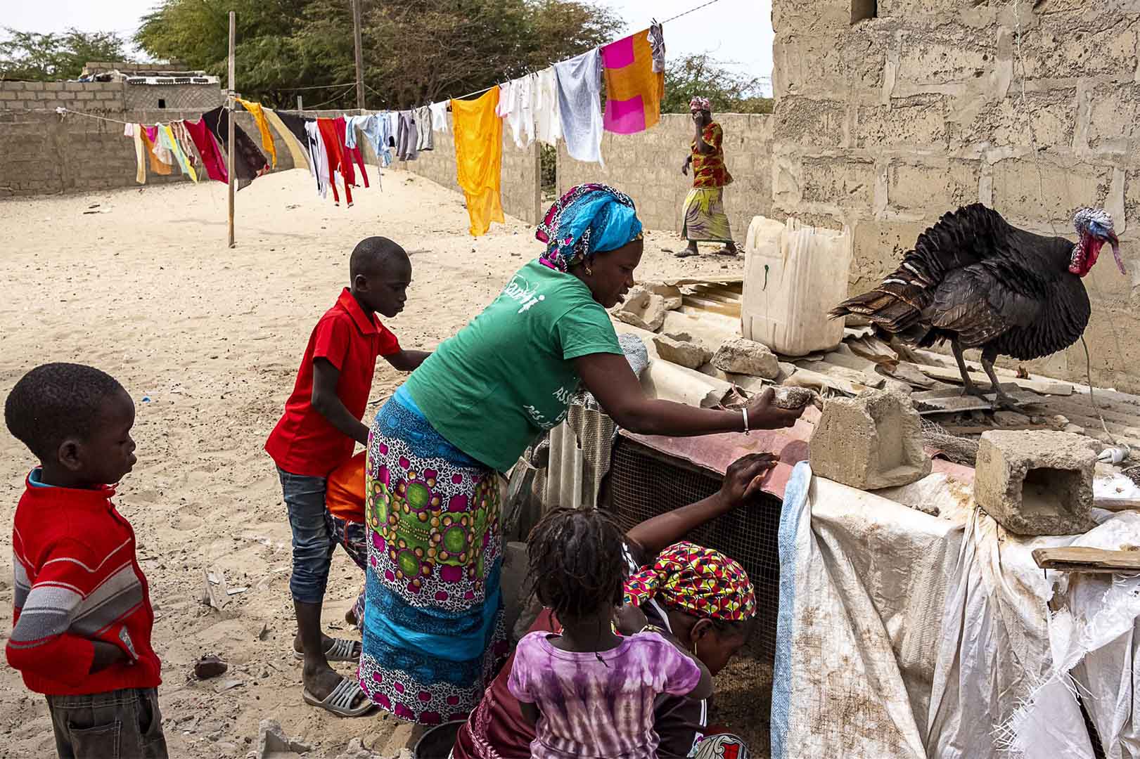 A woman and her children are outside their home checking on their farm animals' cages.