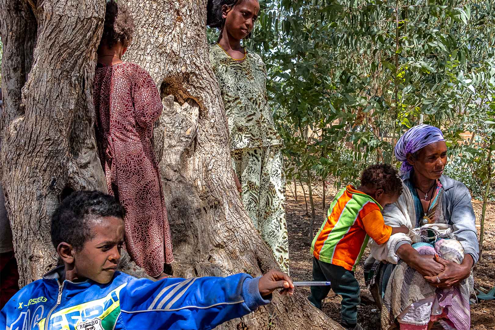 A woman and children sit by a tree.