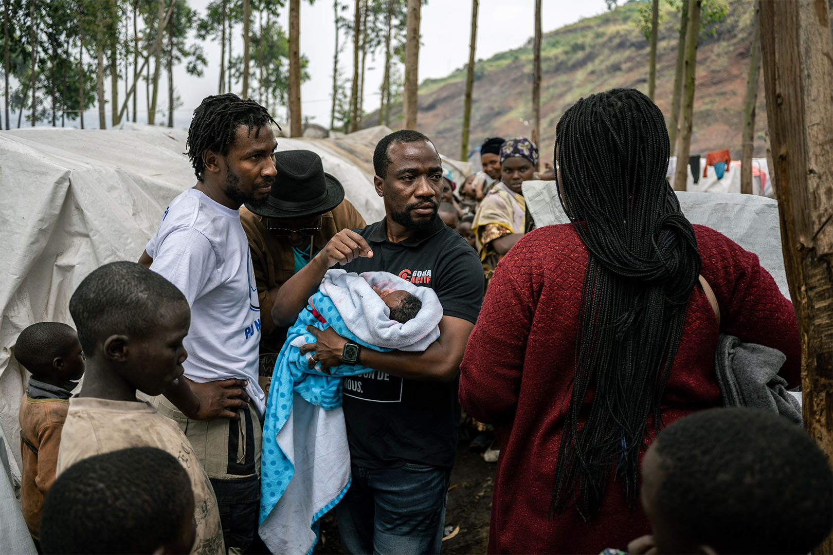 A man surrounded by people holds a baby in his arms. 