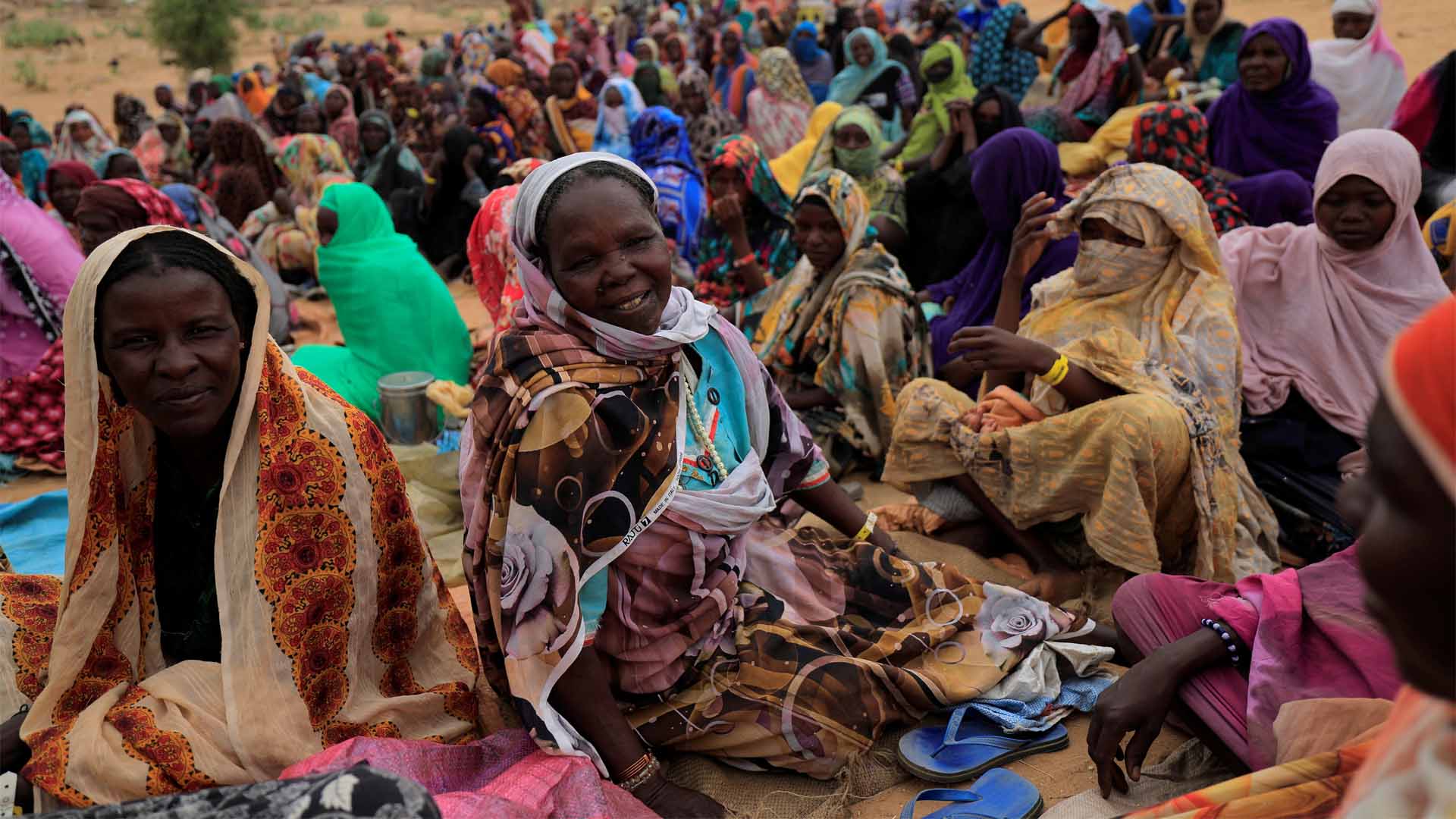 Harana Arabi Souleymane, a Sudanese refugee who is seeking refuge in Chad for a second time, waits to receive food supplements from World Food Programme (WFP) as she chats with other refugees, near the border between Sudan and Chad in Koufroun, Chad, May 11, 2023. She is pictured surrounded by dozens of women, all of which sit on the ground as they wait.