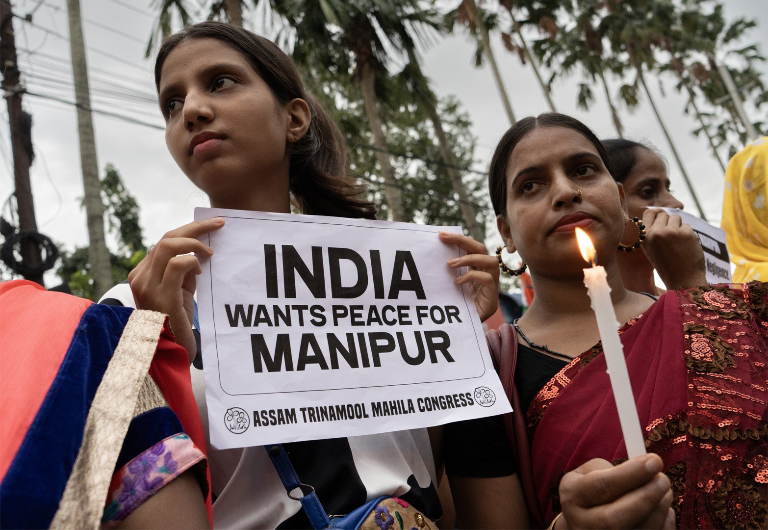 This is a picture taken from a low angle of two women who are holding candles and a paper that reads "India wants peace for Manipur". They are attending a candlelight protest over sexual assault case of two Kuki community women, during ongoing ethnic clashes between Meitei-Kuki community in Manipur, organised by Trinamool Mahila Congress, on July 28, 2023 in Guwahati, India.