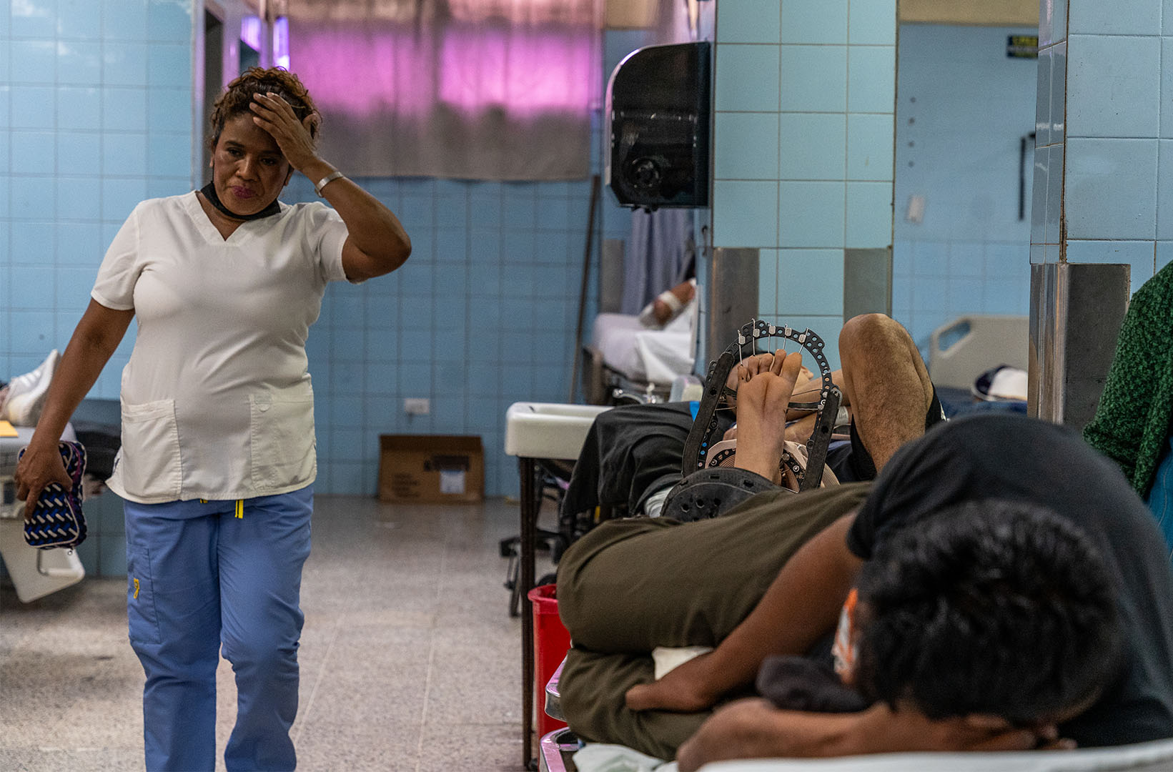 This is a picture of nurse Reina Xiomara Blucha (44), as she is finishing up her morning shift in the emergency department of the ‘Hospital Escuela’. She's pictured walkinf down a hospital hall with her right hand on on her head. On her right are people on a stretcher.