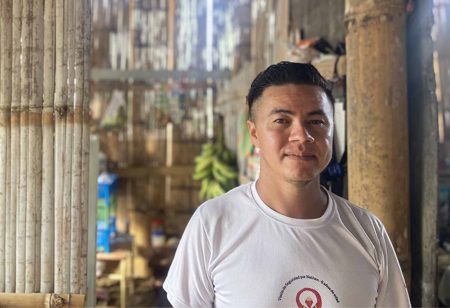 This is a portrait photo of Javier Cevallos in his house in Nueva Esperanza. He's standing in front of a door frame. He wears a white shirt.