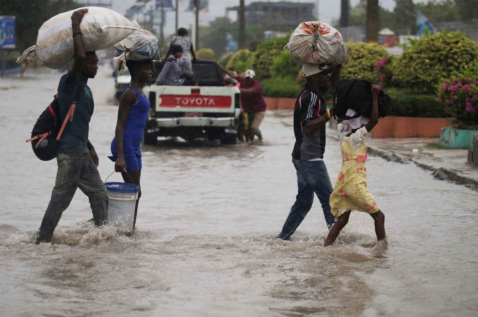 This picture shows four people crossing a flooded street during the passage of Tropical Storm Laura, in Port-au-Prince, Haiti August 23, 2020. They're carrying sacks full of their items.