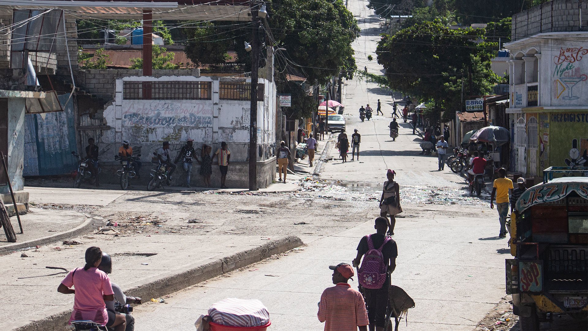 This picture is shows a view of Carrefour-Feuilles, Port-au-Prince. People are seen walking on the streets and others are leaning against a wall. 