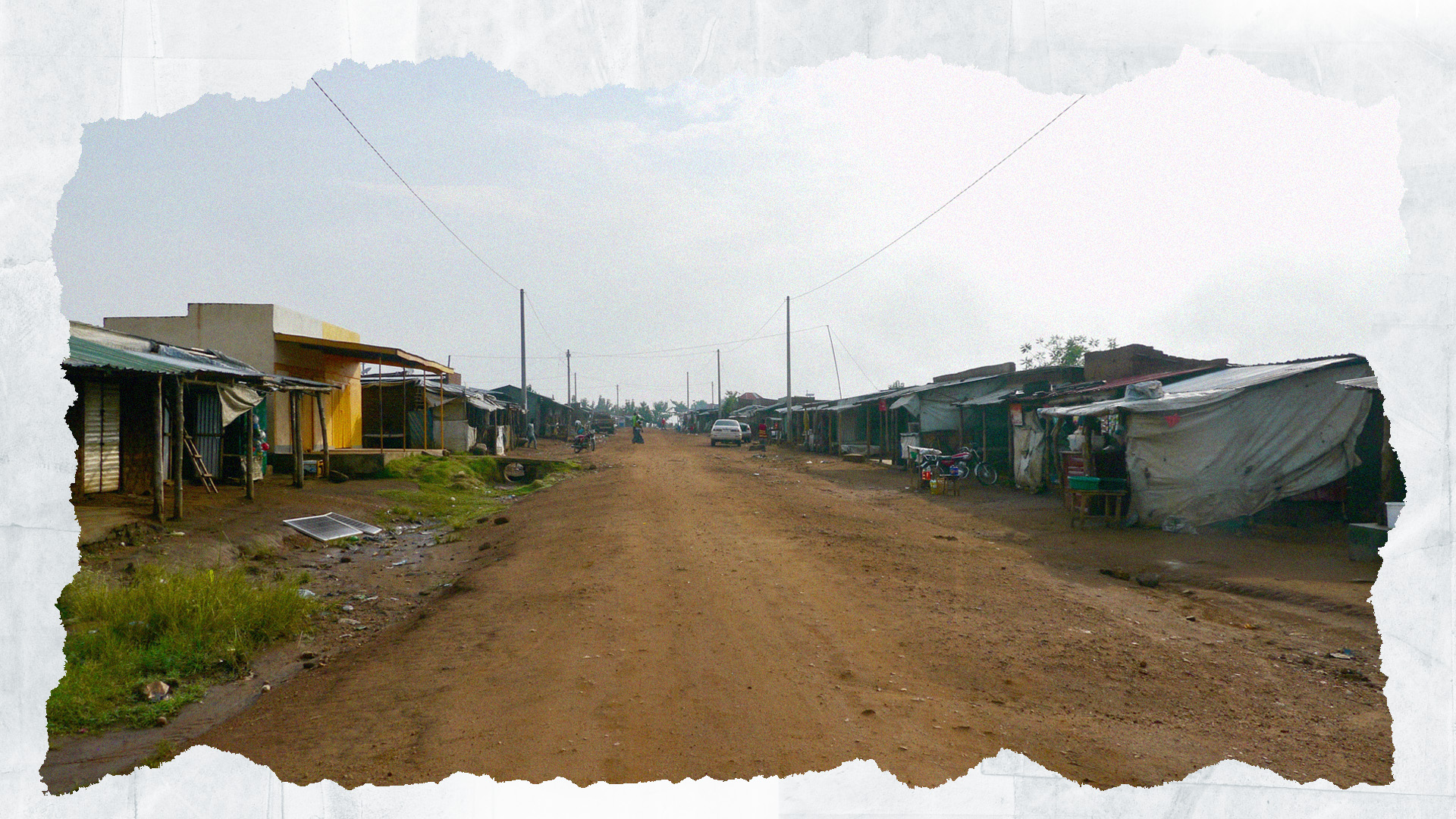 An uneven dirt road runs past shops selling dried goods and essential items in Bidi Bidi refugee settlement, empty in the early morning. August 2023.