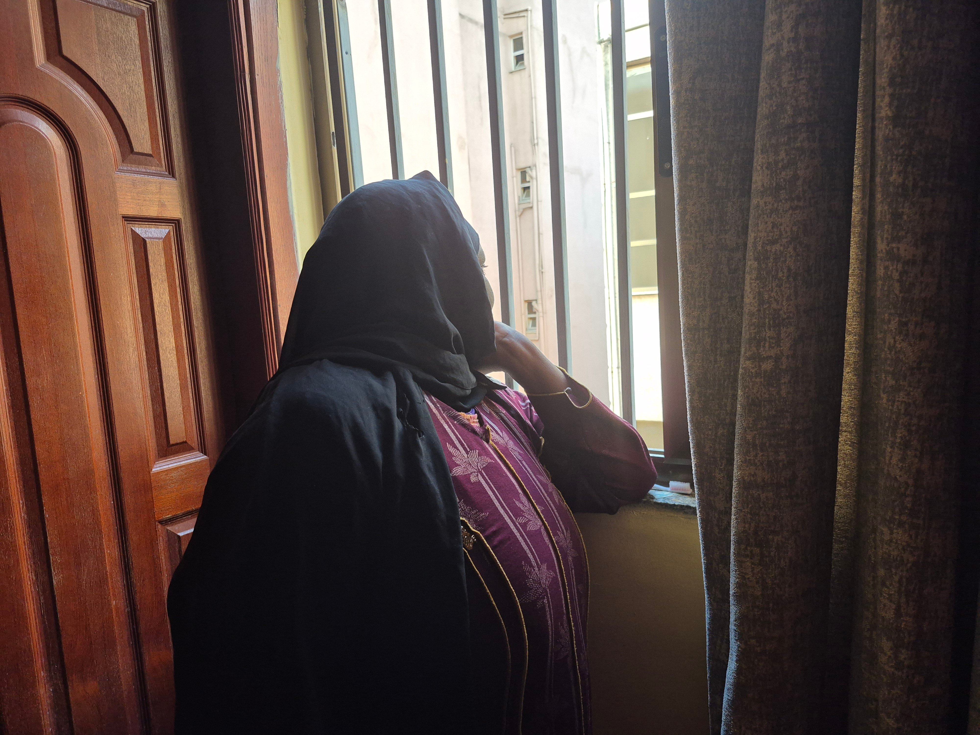 A Sudanese refugee looks out the window of a home. She  rarely leaves her house in Addis Ababa because she fears being arrested for not renewing her visa. 