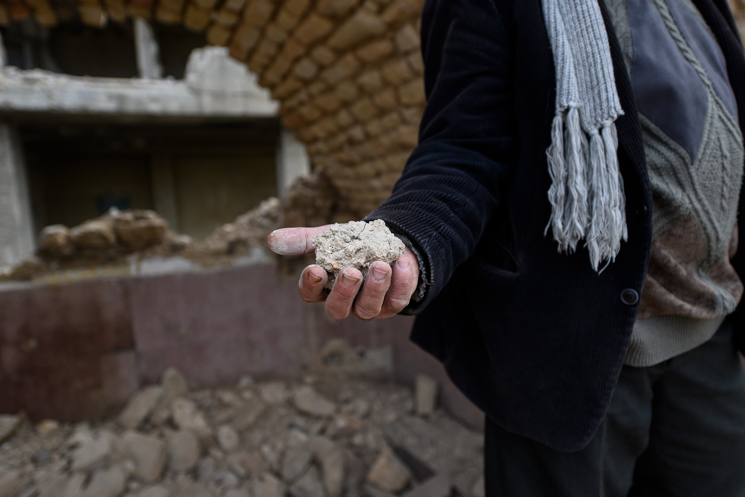 A close up of the hand of Badr el-Din Mouhanna as he holds on two some rubble.