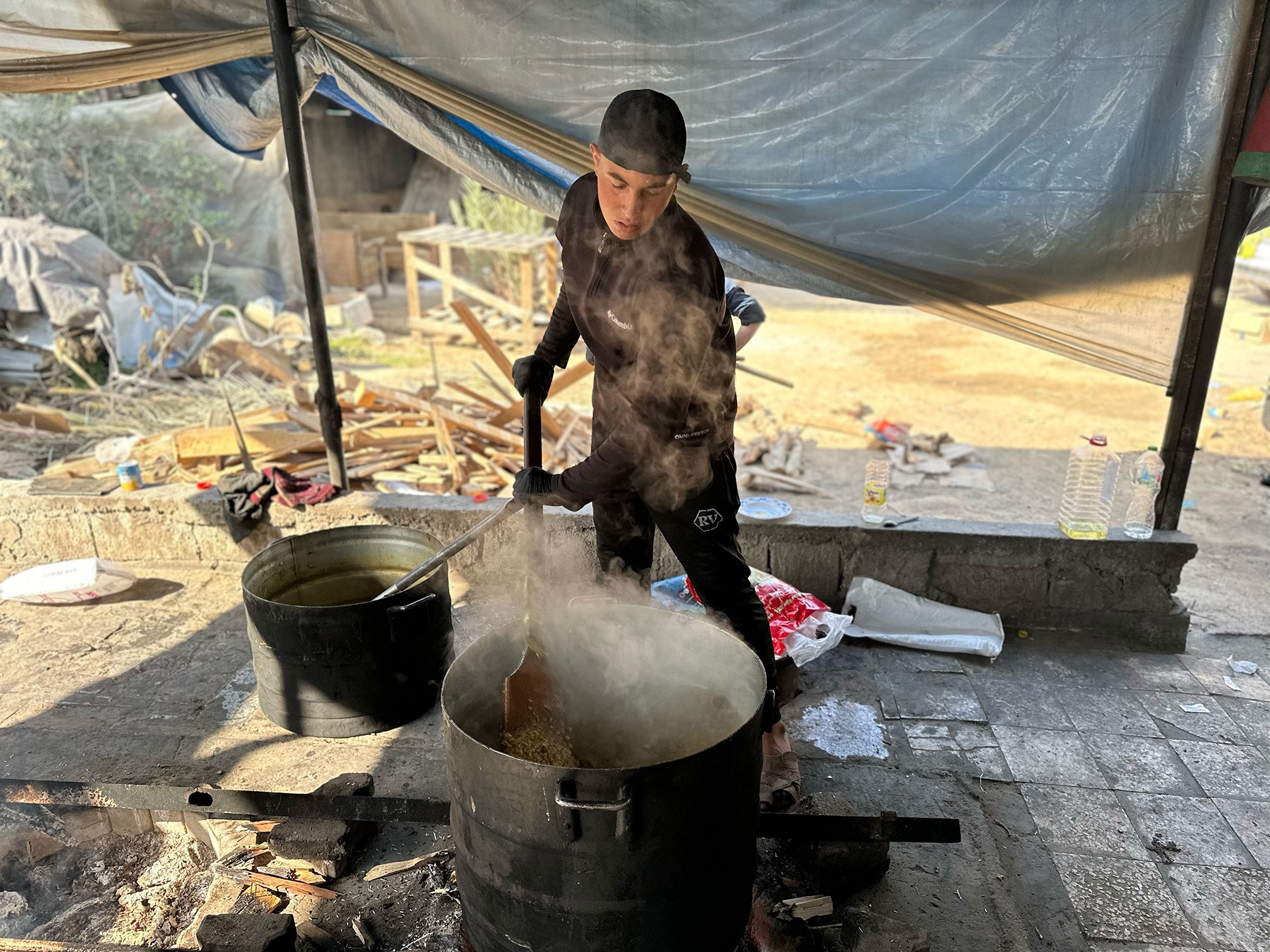 A person stirs food in a large pot at a community kitchen.