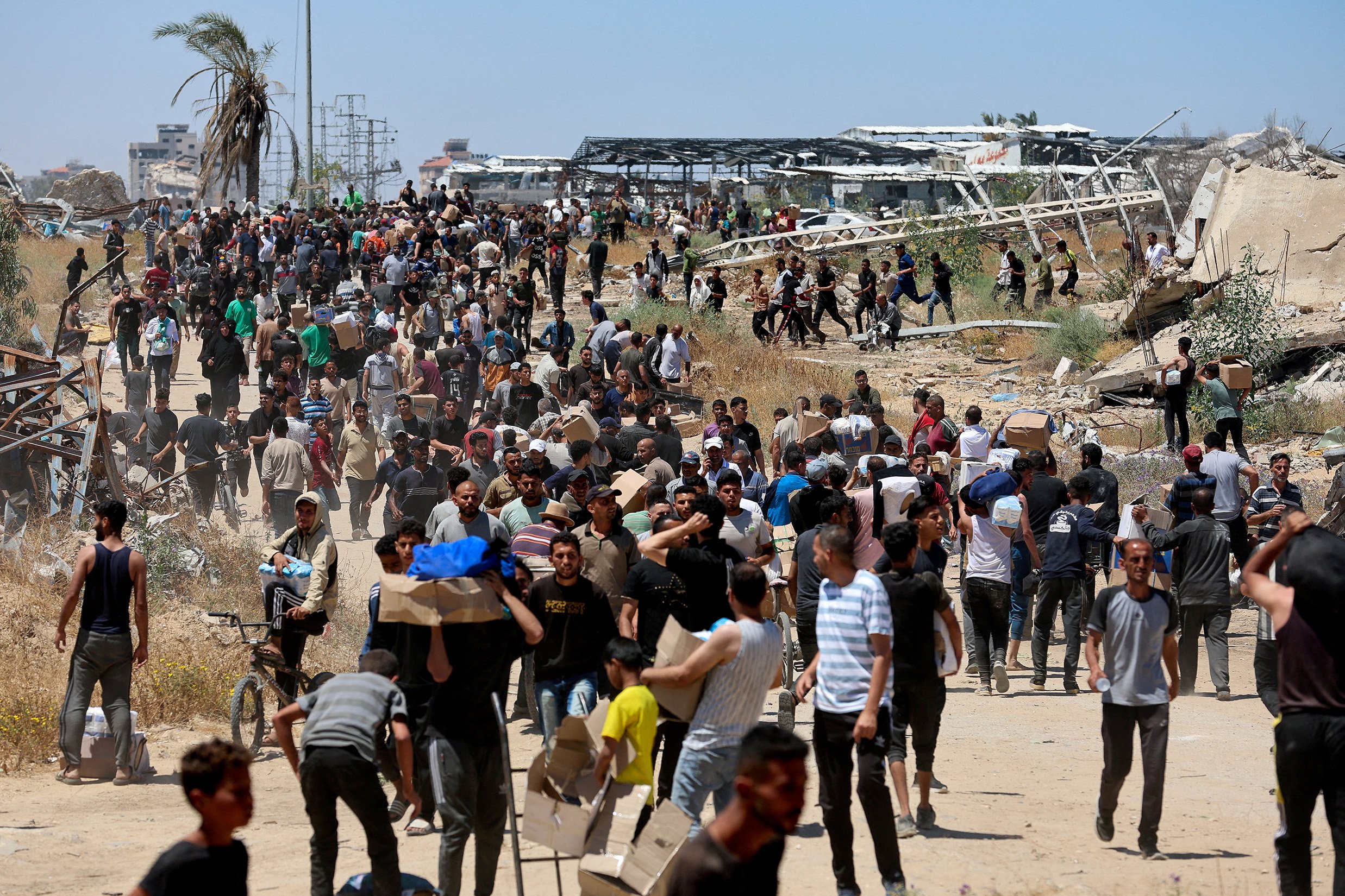 People walk as Palestinians receive aid supplies from the U.S.-backed Gaza Humanitarian Foundation, in the central Gaza Strip, May 29, 2025.