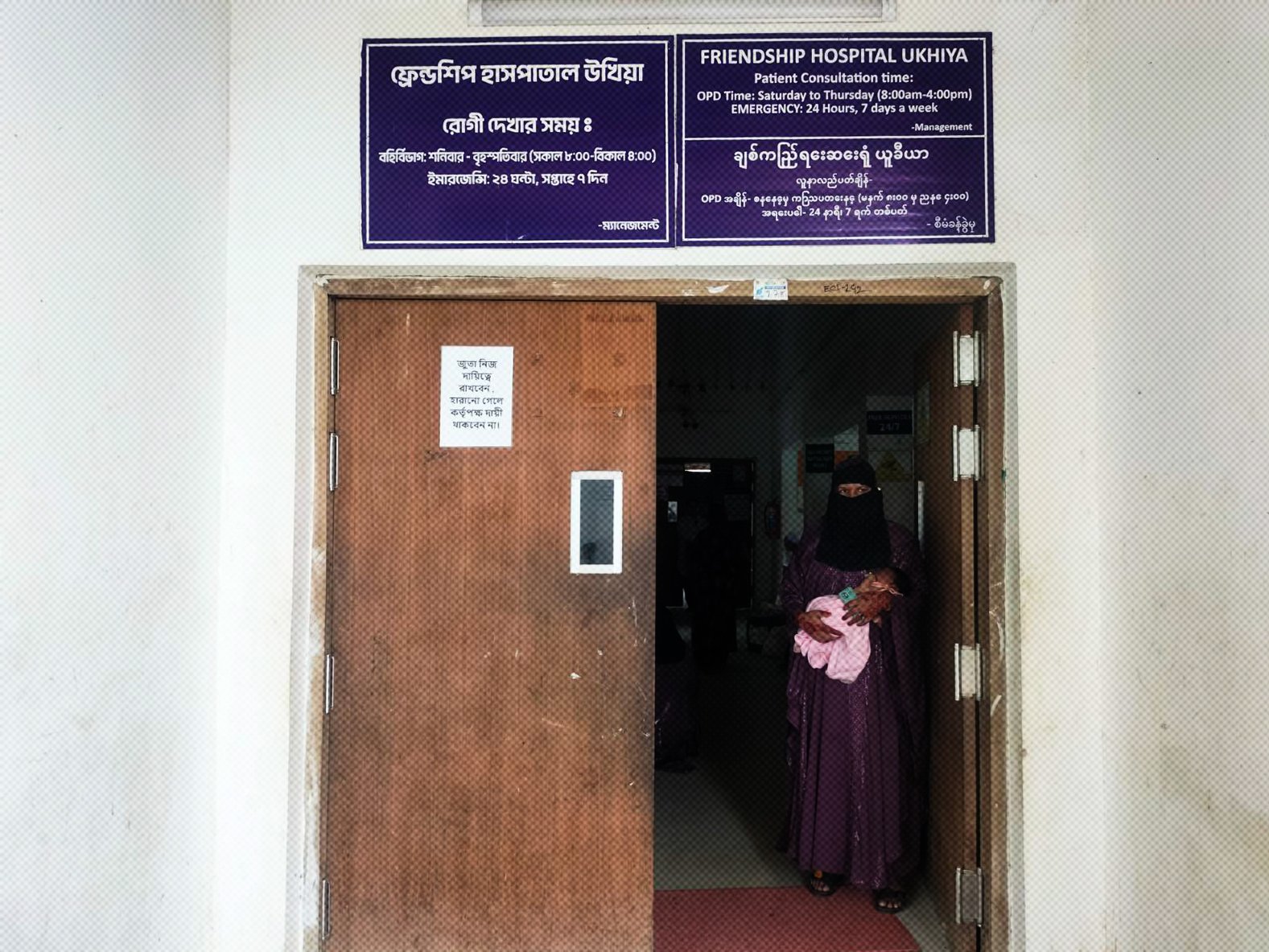 A woman holding a baby stands at the frame of a door at the Friendship Hospital Ukhiya in Myanmar