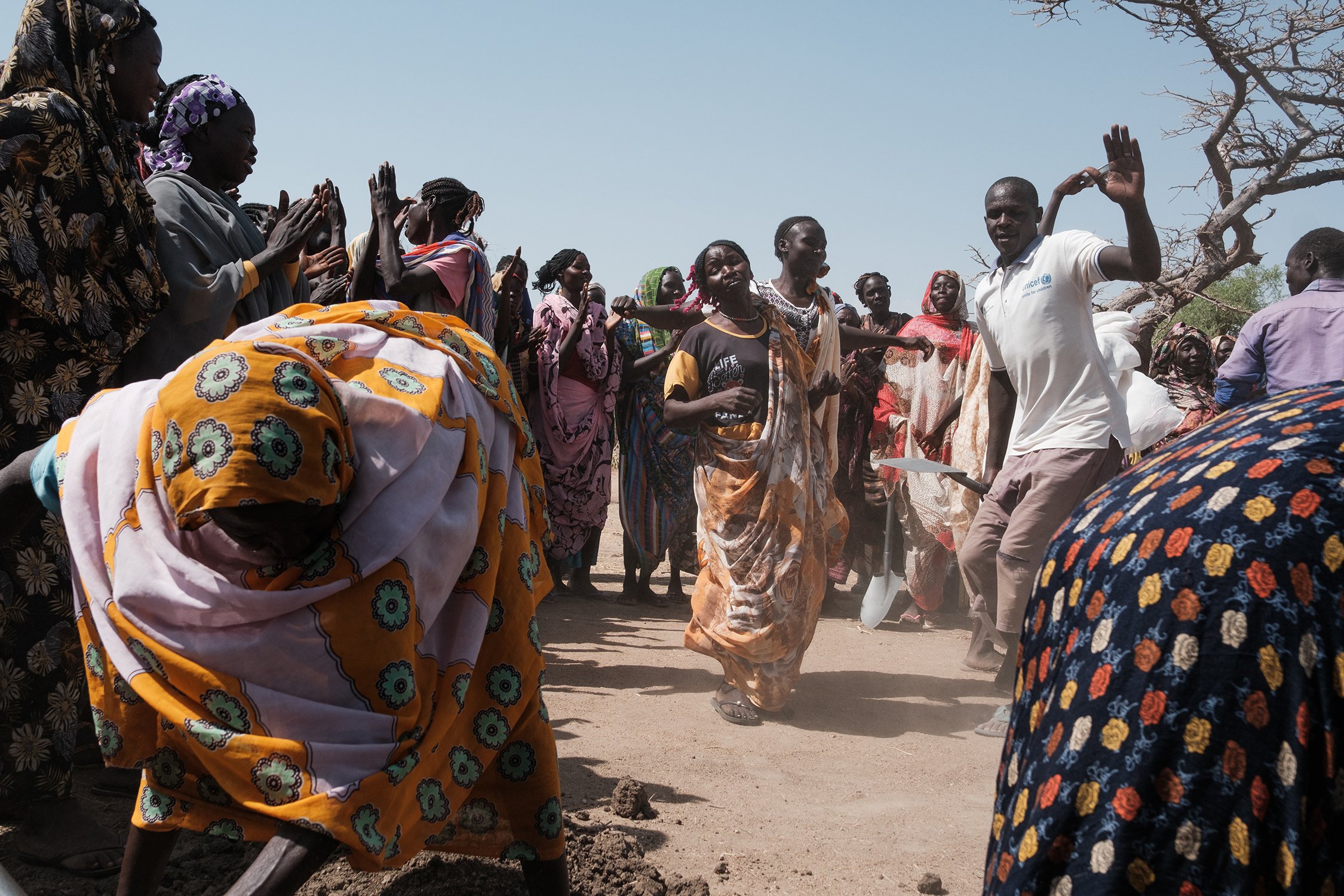 Mudsir Muhammad (in the white t-shirt) dances with residents of Al-Hilu displacement camp as they dig a trench to bring water from a nearby town, on 23 April 2025.