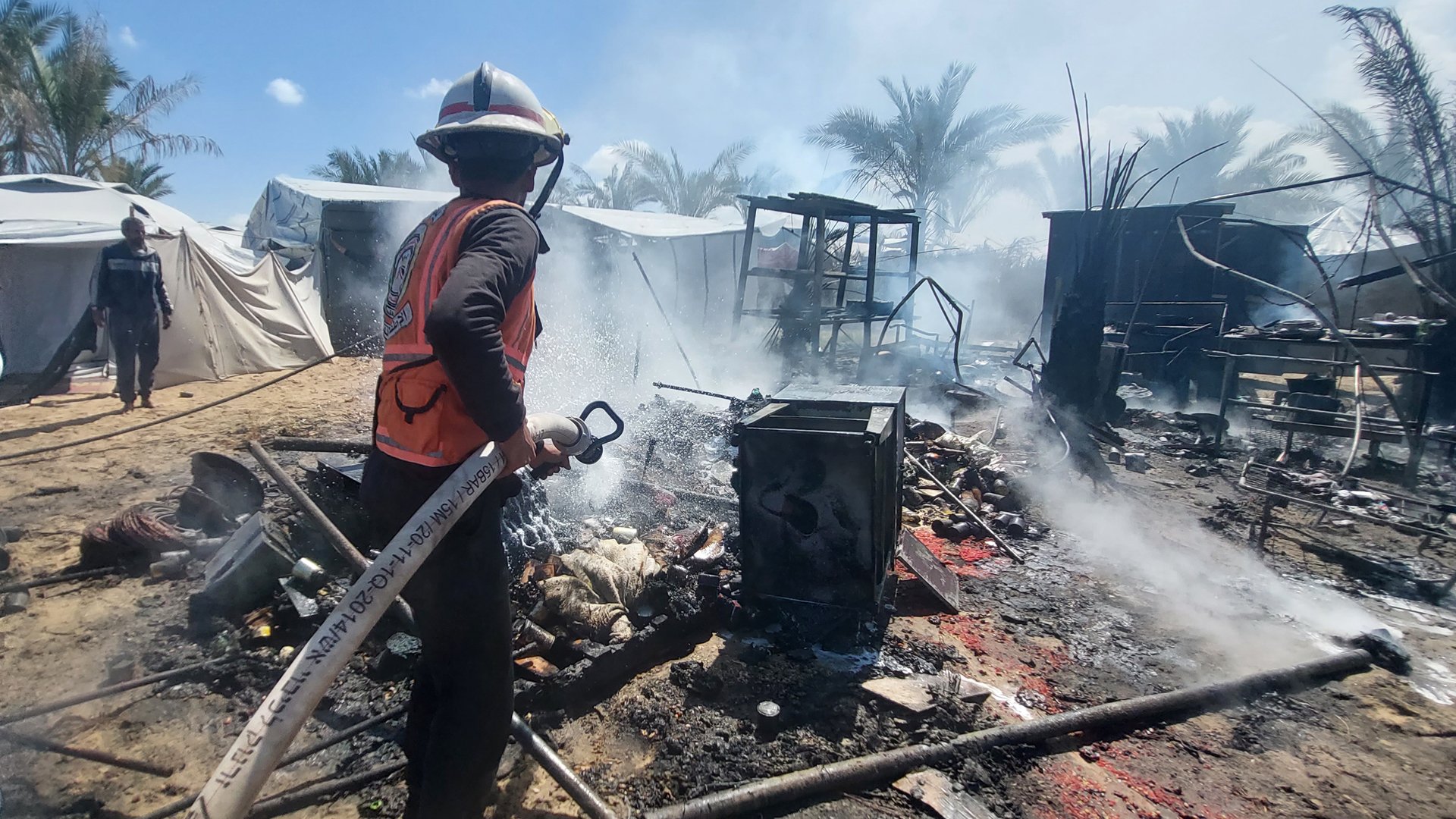 A member of Ahmed Radwan’s team douses the remains of tents reduced to ash by an Israeli missile strike with water to put out the flames.