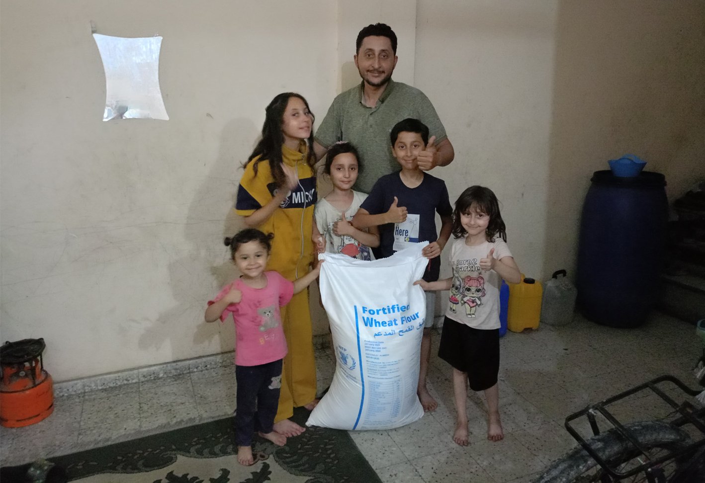 Rasha Abou Jalal’s husband, Abdullah, and their five children with the sack of flour they received from the UN’s World Food Programme.