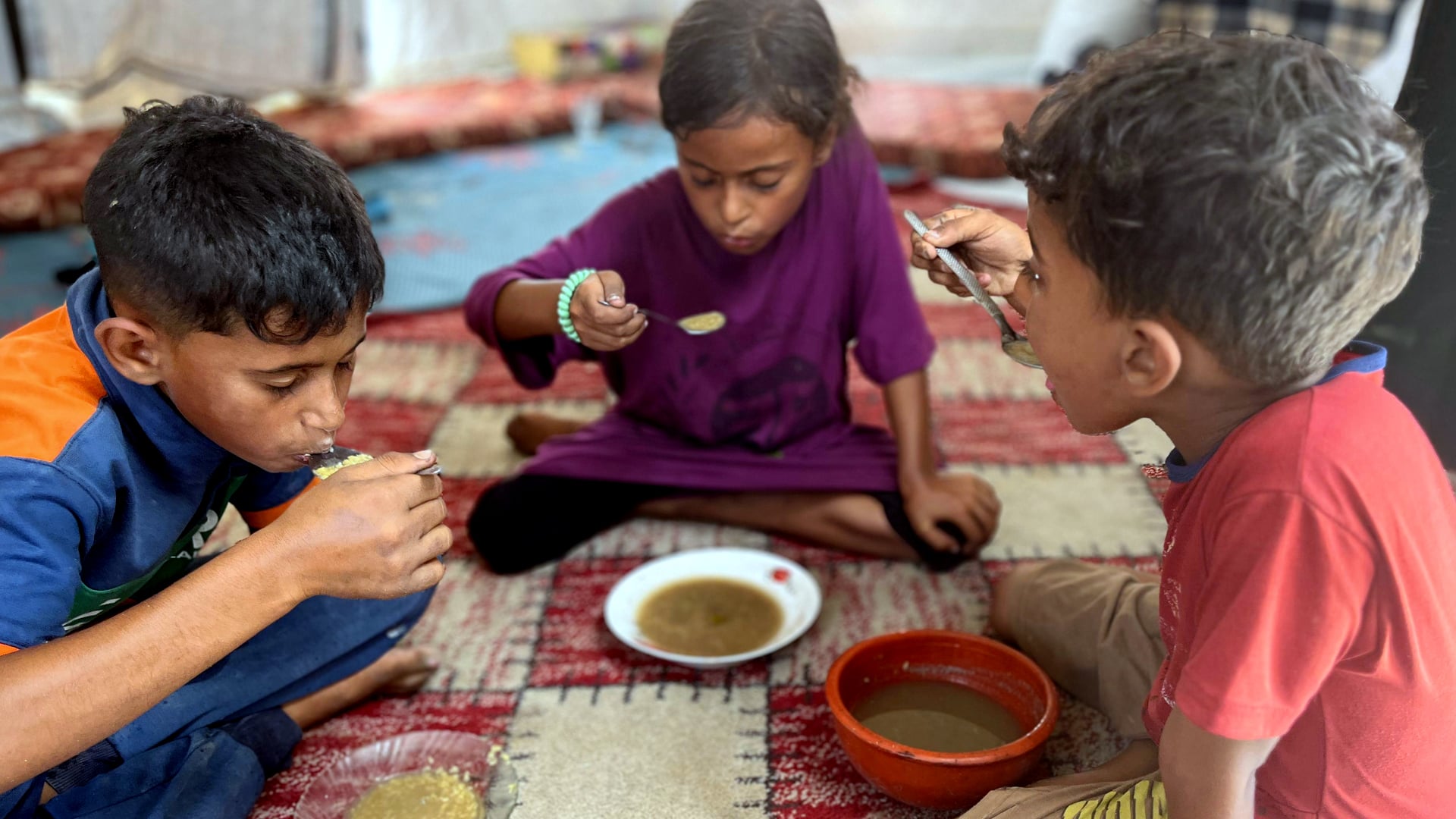Three of Sahar al-Qassas' children eating the thin lentil soup she prepared.
