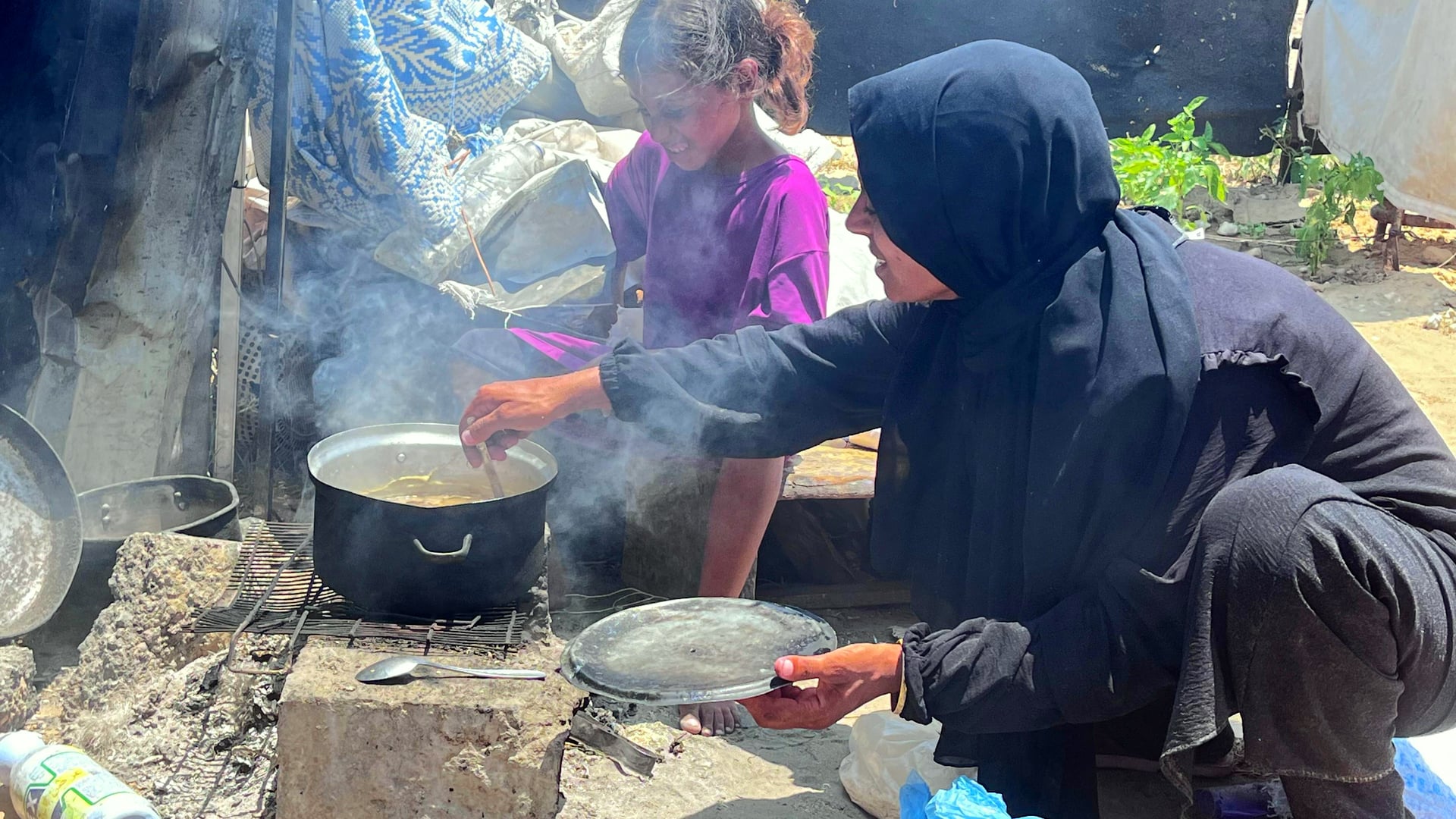 Sahar al-Qassas and her eight-year-old daughter Nesma preparing thin lentil soup and stoking the cooking fire.