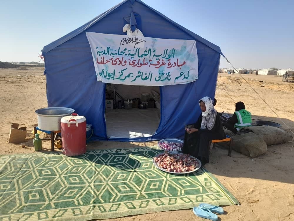A large blue tent with a sign on the front in an arid landscape, a mat lays outside of the tent door