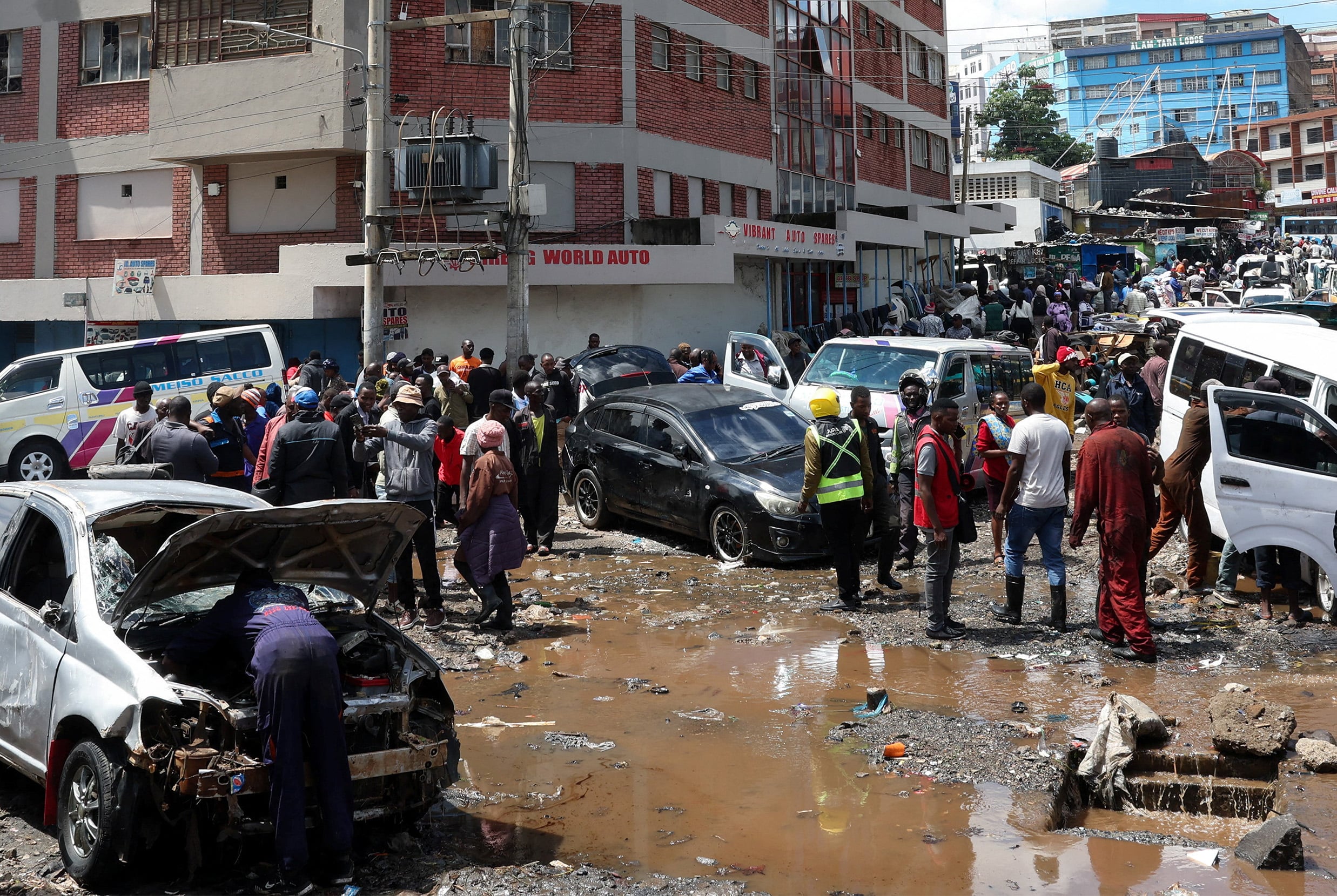 People stand around destroyed vehicles following flash floods caused by heavy rainfall in the Grogan area, popular for automotive workshops and secondhand spare parts, in downtown Nairobi, Kenya, March 7, 2026. 