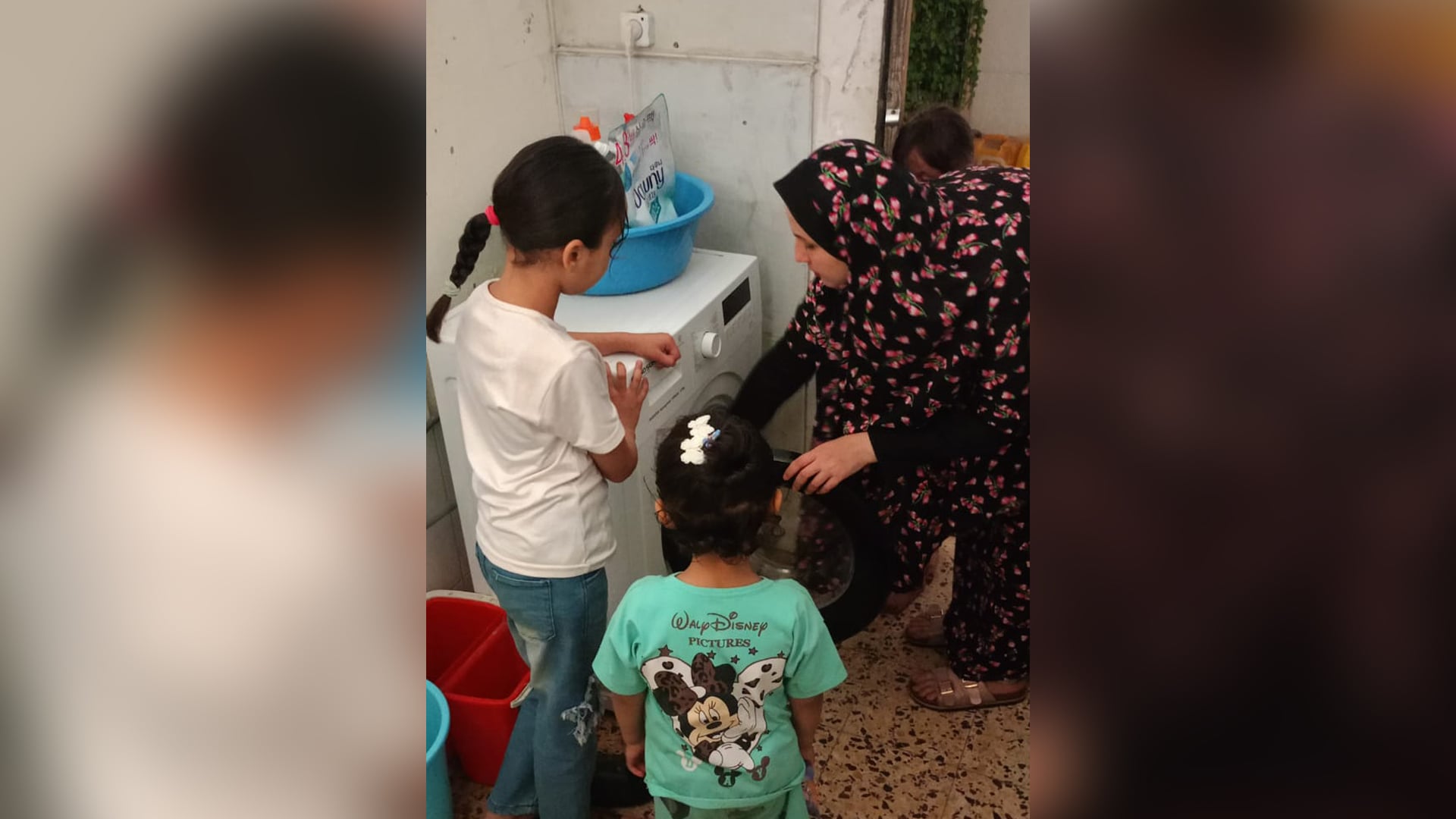 Rasha Abou Jalal puts clothes inside a washing machine as her children look on.