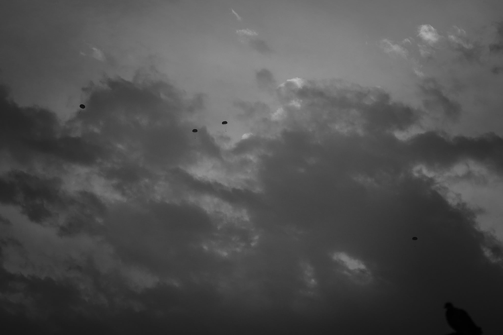 A black and white photo of the sky showing airdrops of weapons and medicine into El Fasher to supply a military base located inside the besieged city.