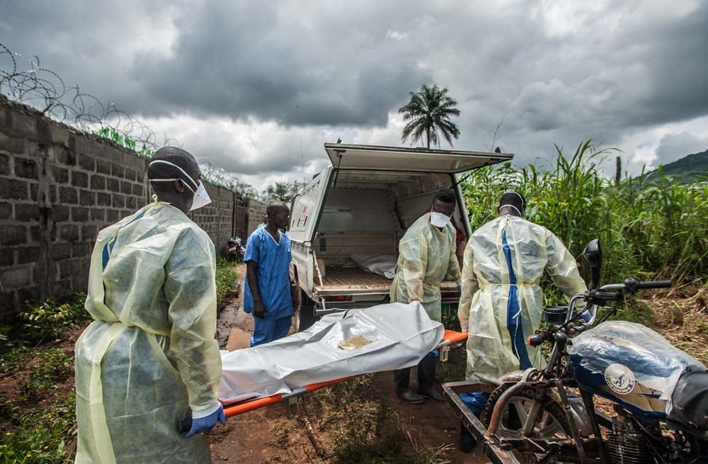 Burials workers in protective gear load a covered body on a stretcher.