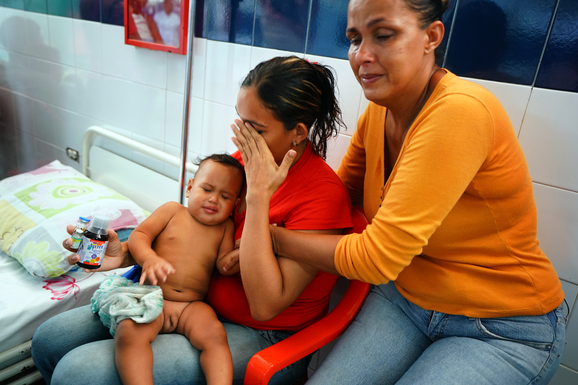 A woman comforts a woman holding a child on a hospital bed