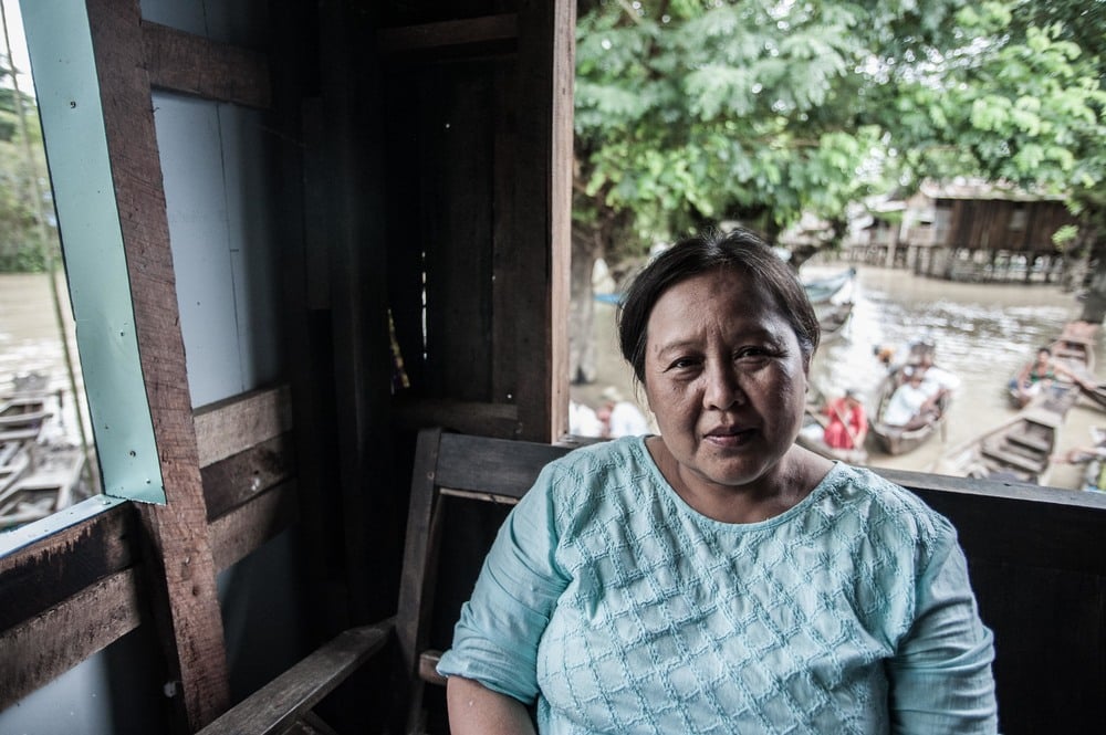 Naw Eh Eh Wah, a Baptist church minister in the village of Nwe Ni Chaung of Myanmar, sits in a room with a view to many people paddling in boats behind her.