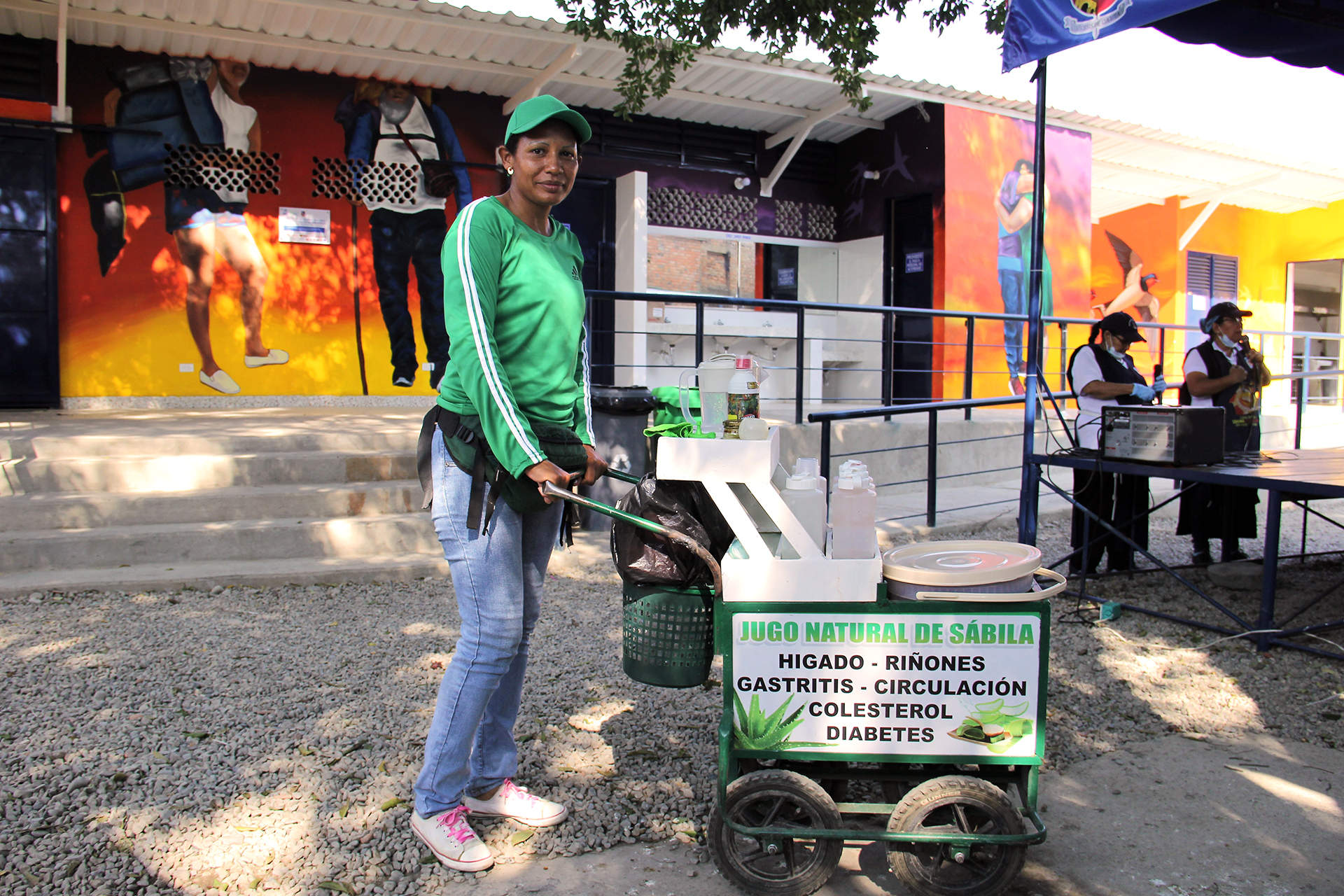 A woman stands in the shade with her cart selling Aloe Vera juice