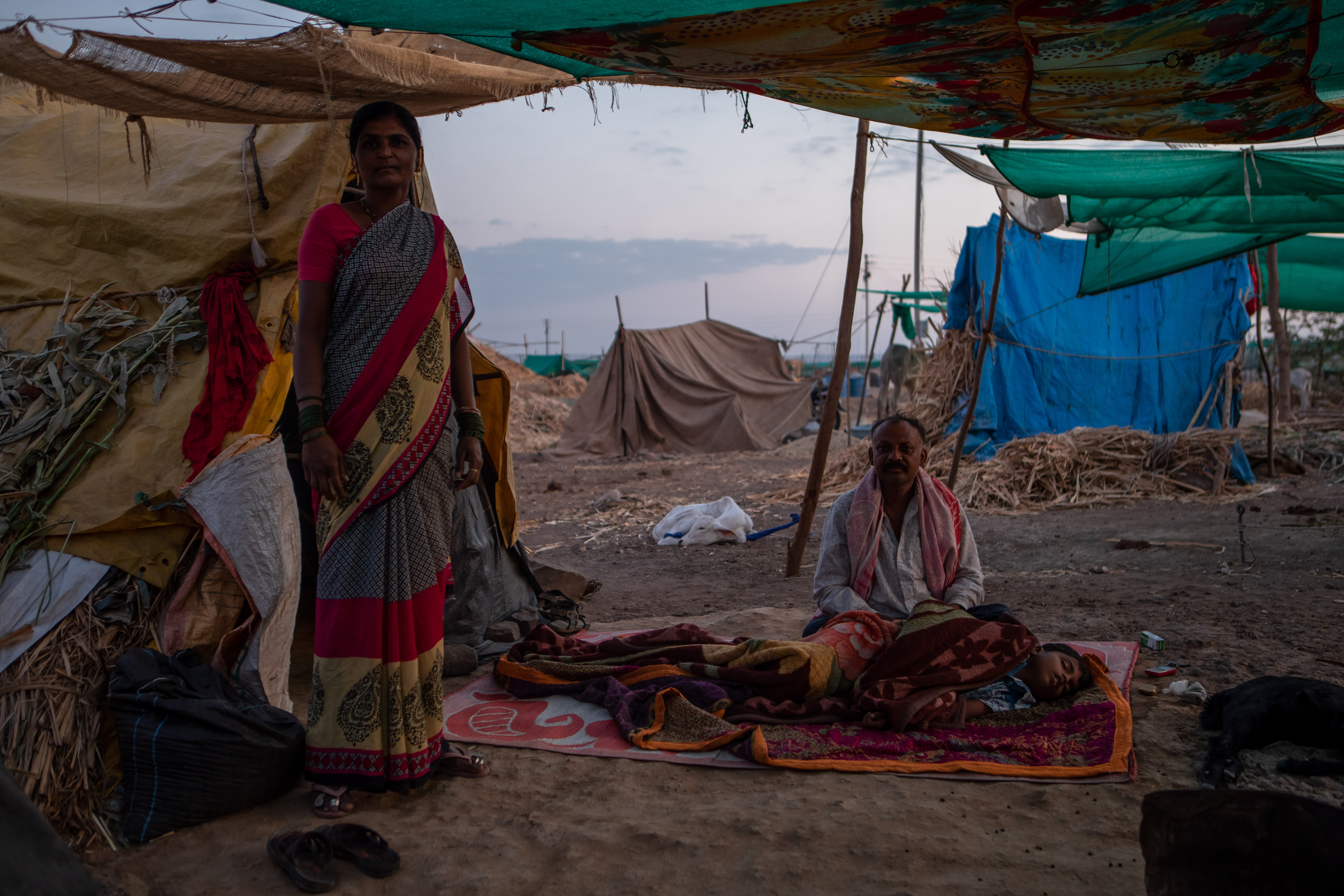 A man sitting on the floor and a woman standing in a makeshift settlement