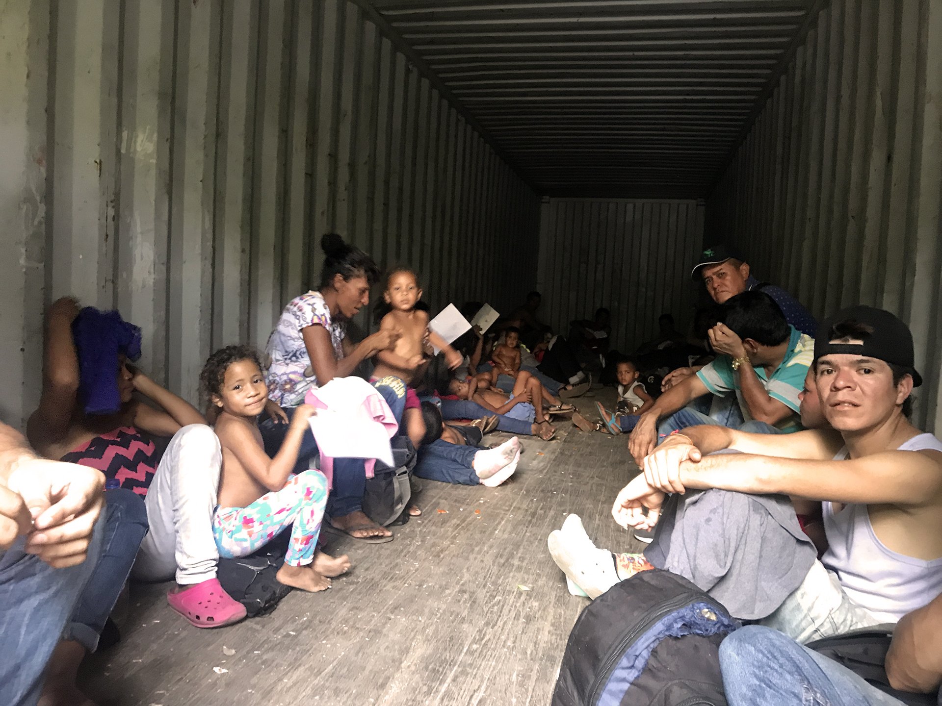 A group of men, women, and children in the back of a shipping lorry