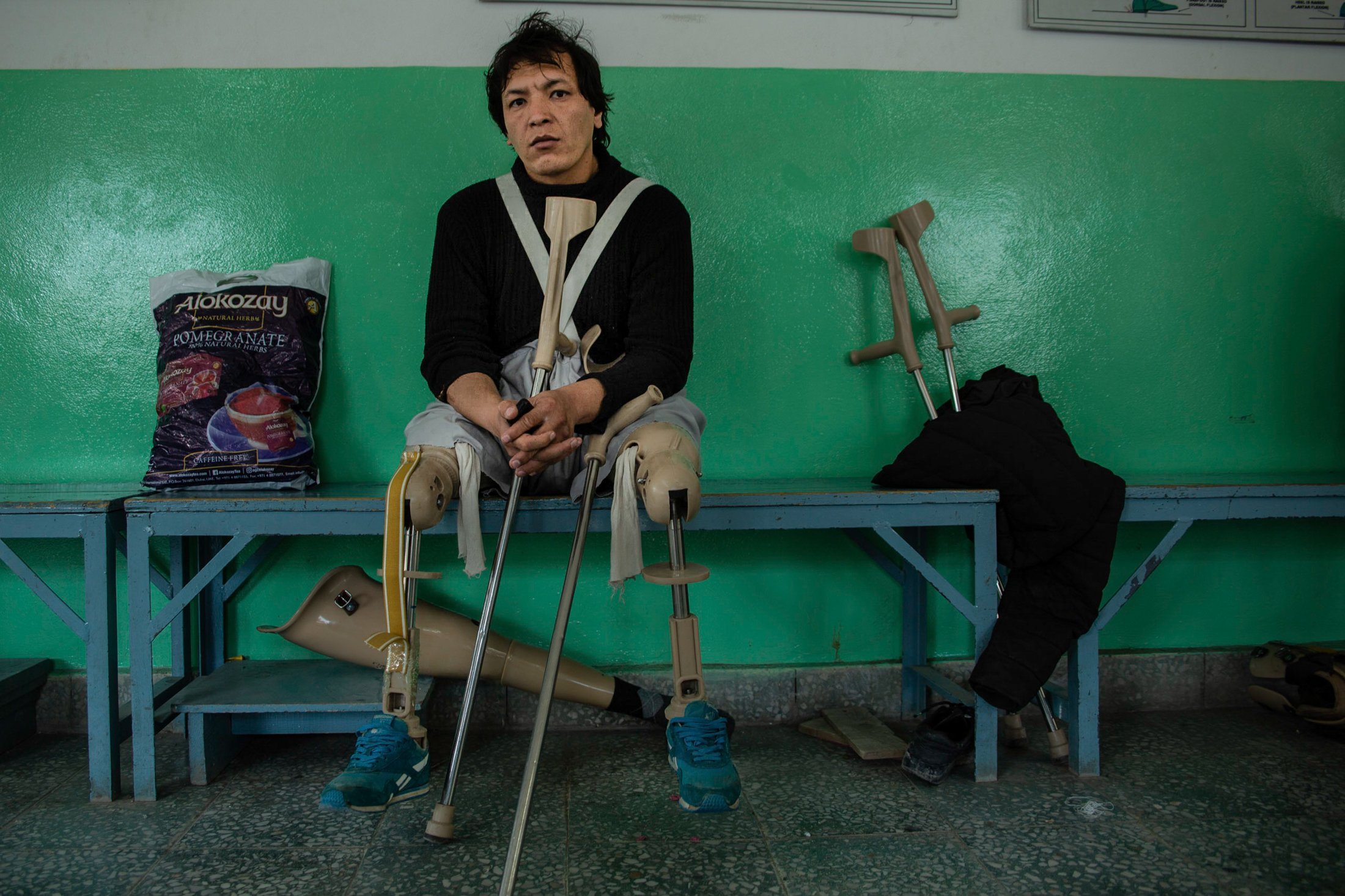 A man with crutches sits on a bench in a medical facility