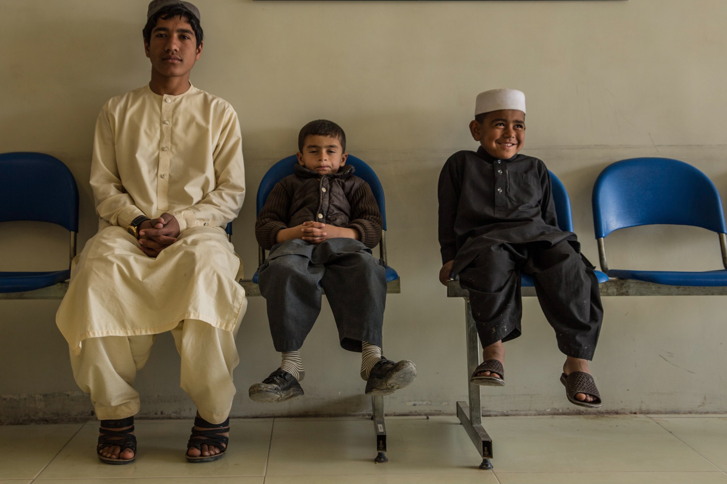 Photo of three children on a bench in a hospital in Afghanistan, one is smiling