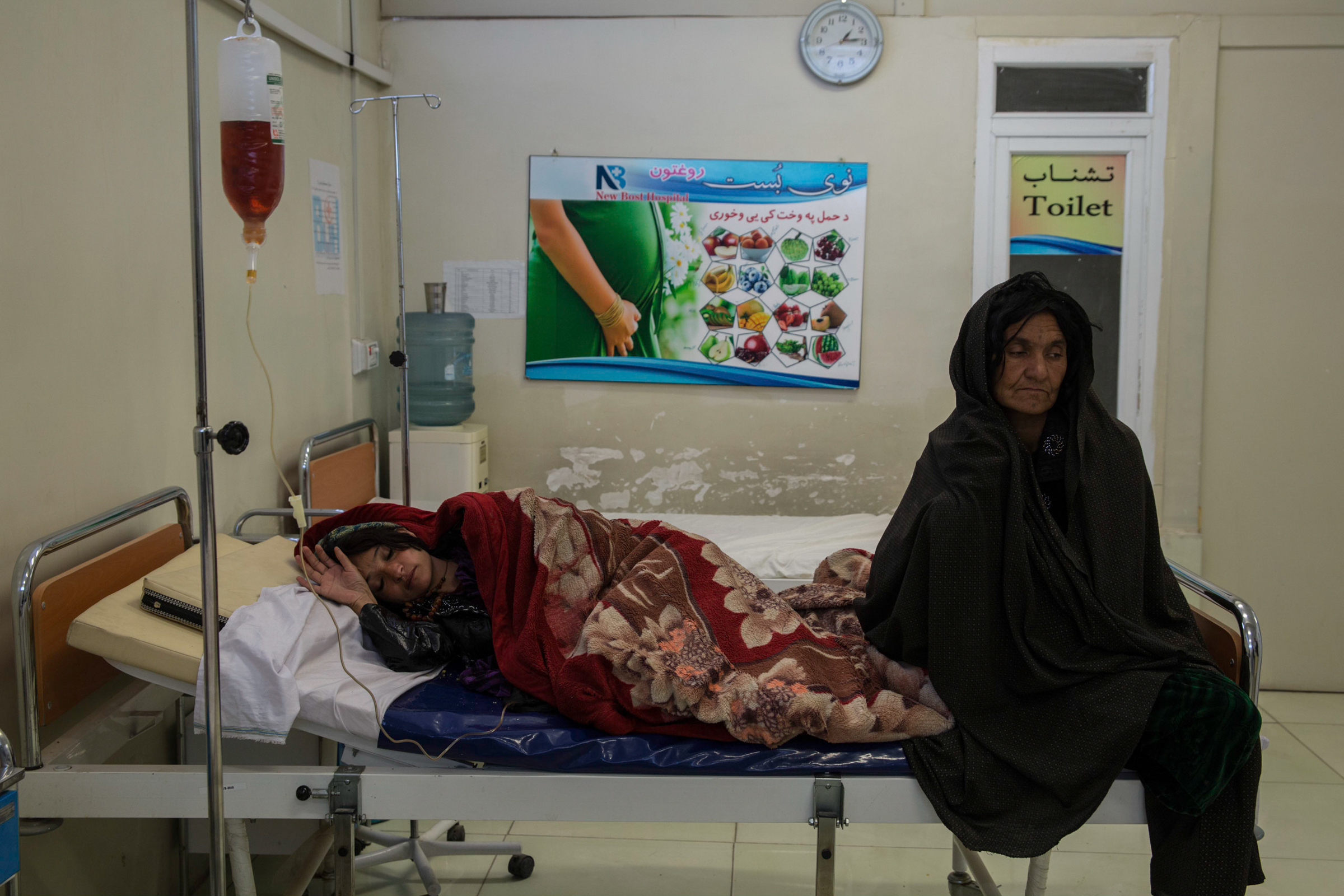 Photo of a woman in Afghanistan in a hospital bed and another sitting at the end of the bed.