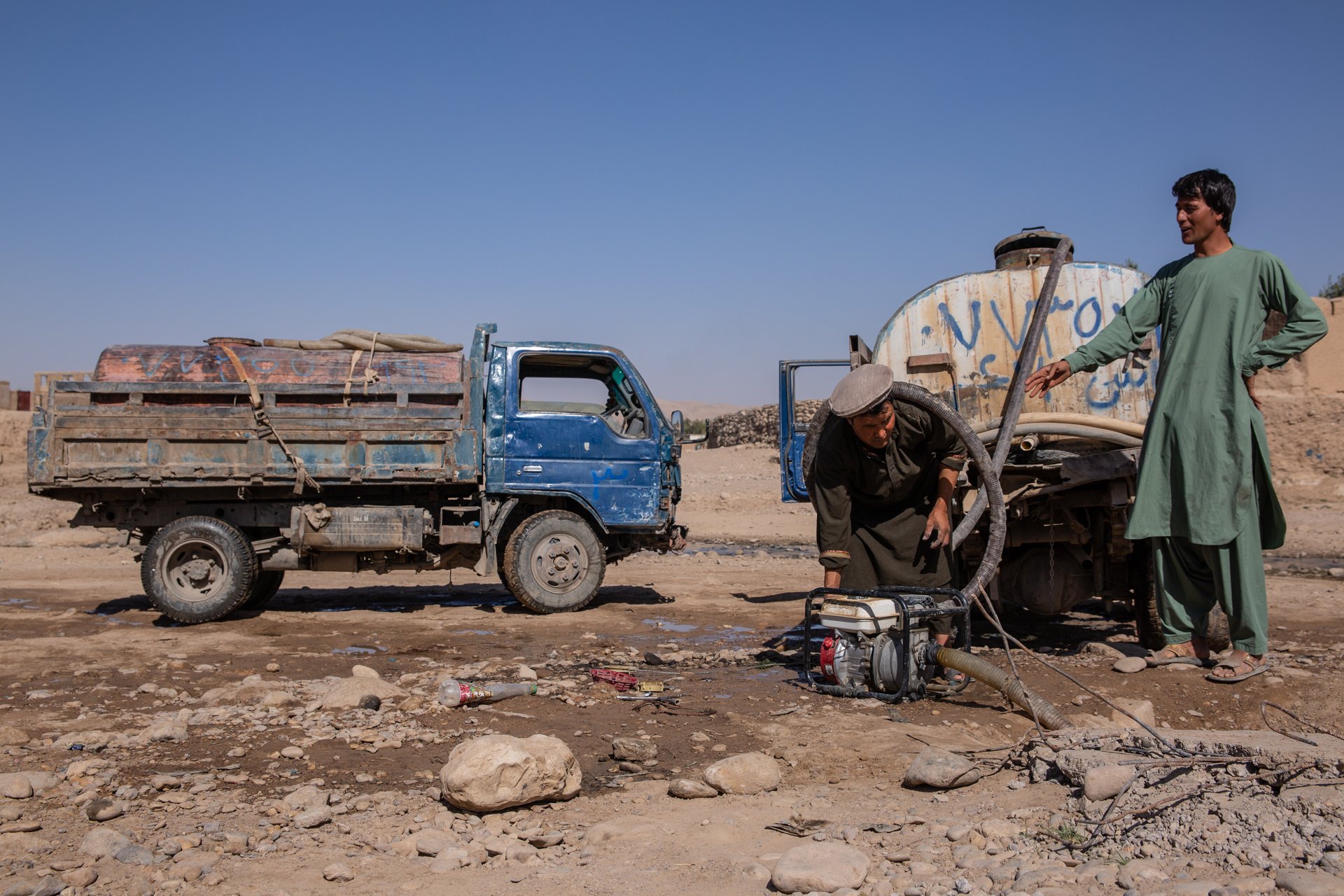 Two men in Afghanistan with trucks and a water pump in the dirt