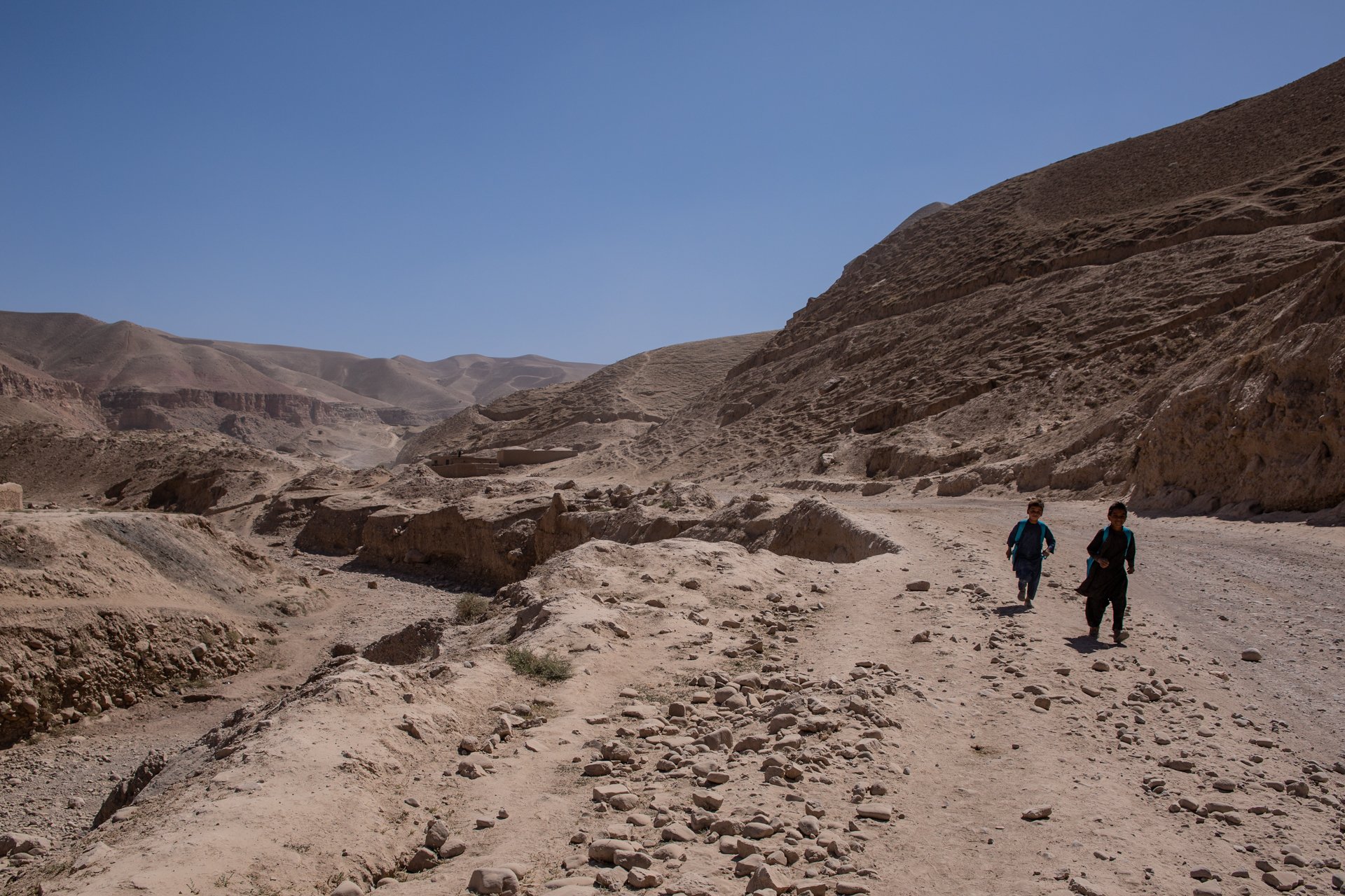 Two children walk in a completely dry, sandy mountain area in Afghanistan