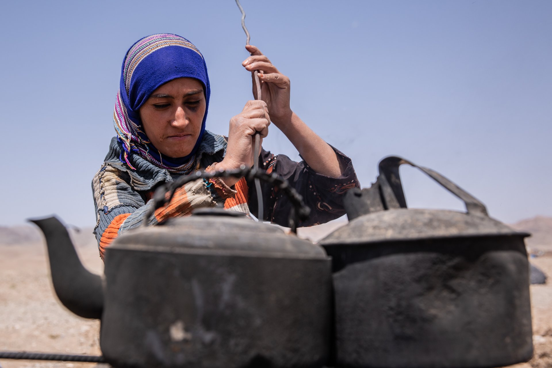 A woman behind two tea pots in a camp in Afghanistan