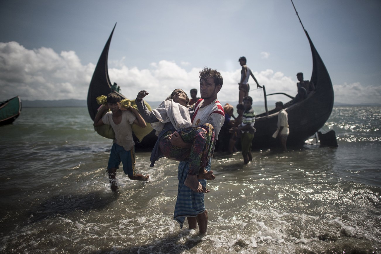 A Bangladeshi man helps Rohingya Muslim refugees to disembark from a boat on the Bangladeshi shoreline of the Naf river after crossing the border from Myanmar in Teknaf on 30 September 2017.