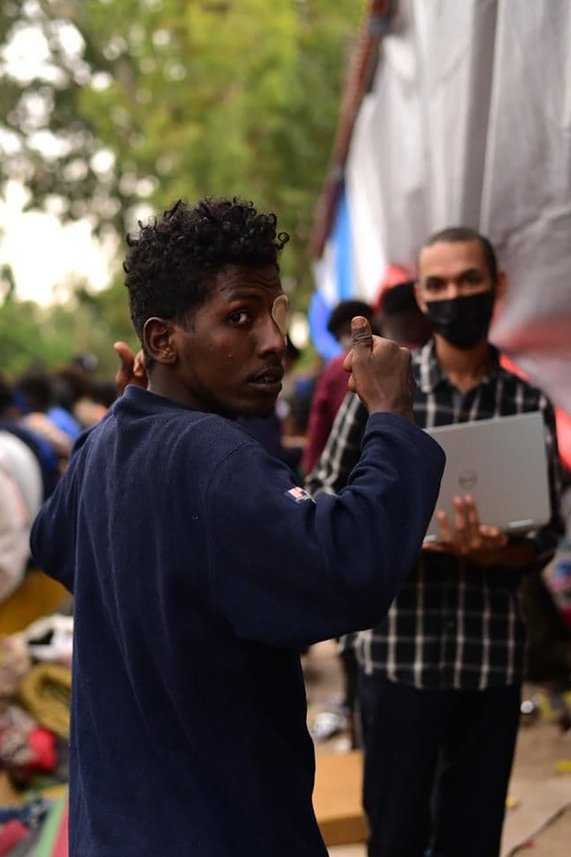 The author (background) records needs on his laptop during a visit to the makeshift encampment outside the UNHCR community centre in October. 