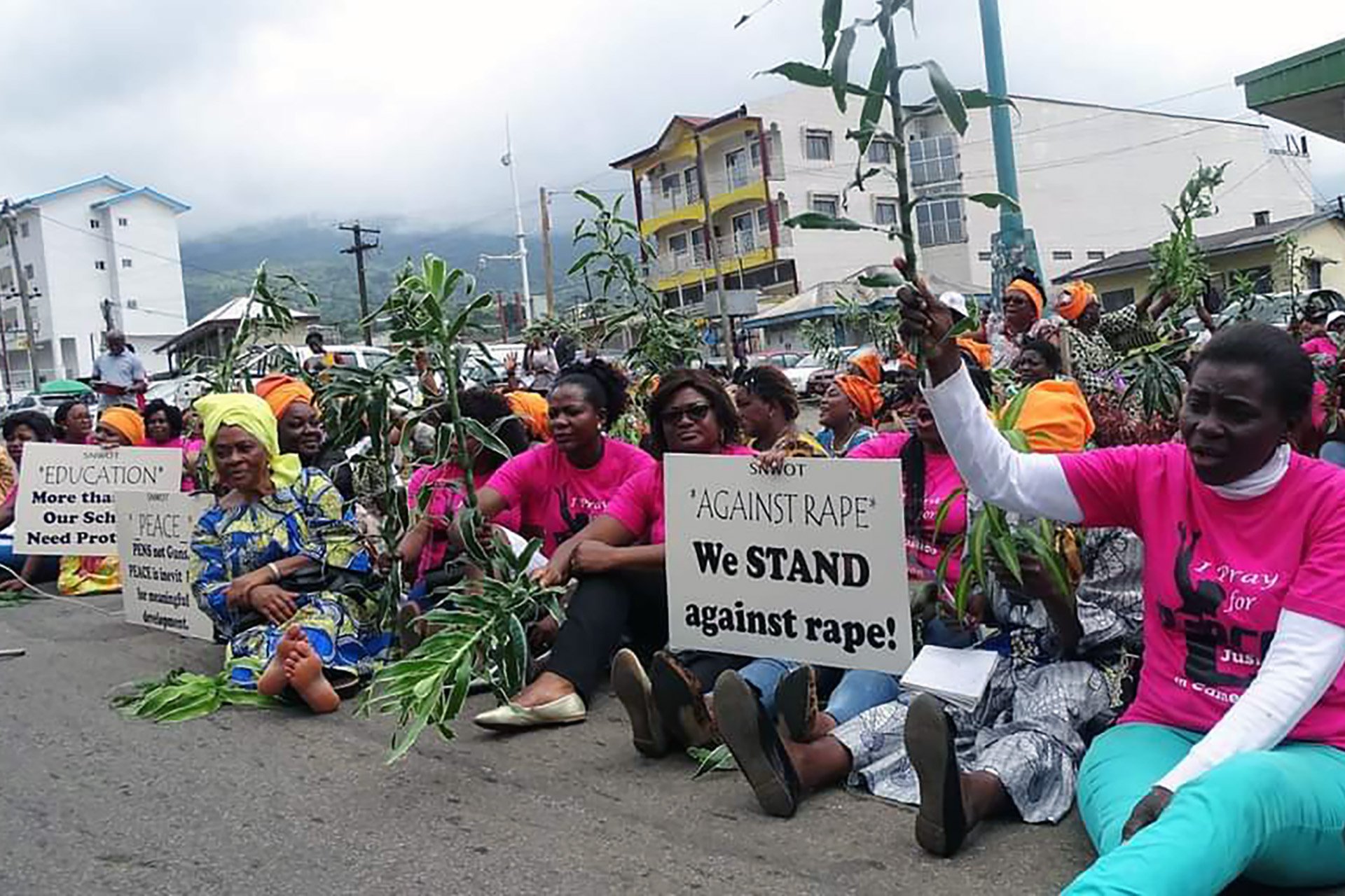 A large group of women sit on the ground and hold signs advocating for peace.