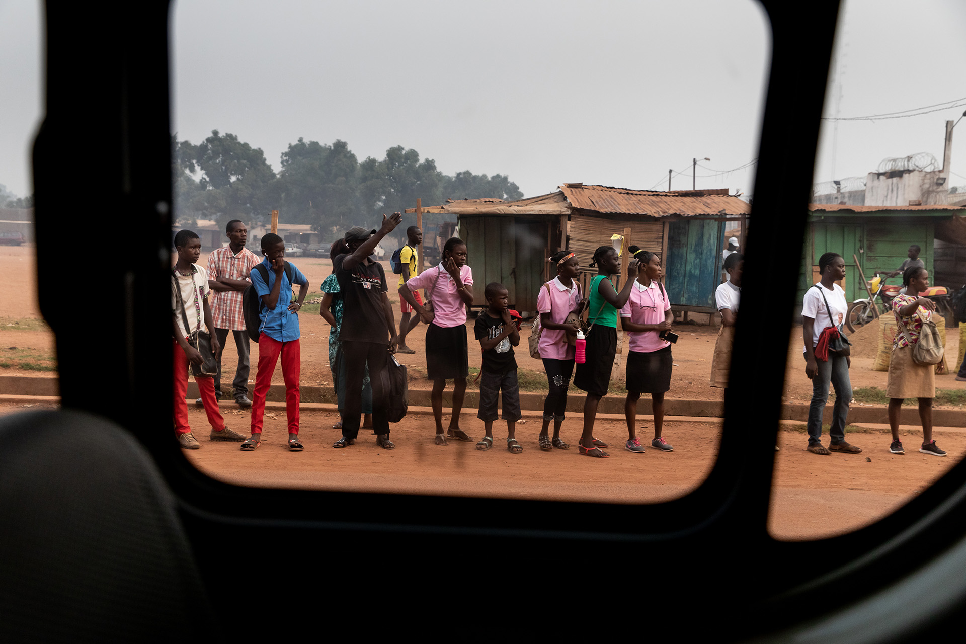 Through the window of a vehicle, residents of Bangui are seen standing by the roadside. 