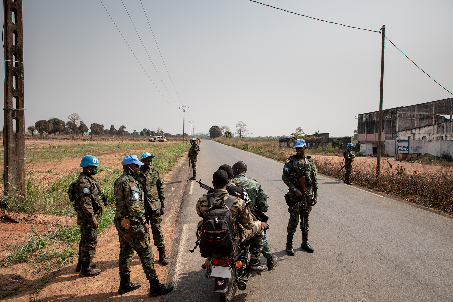 Rwandan peacekeepers stand across a highway in the sun.